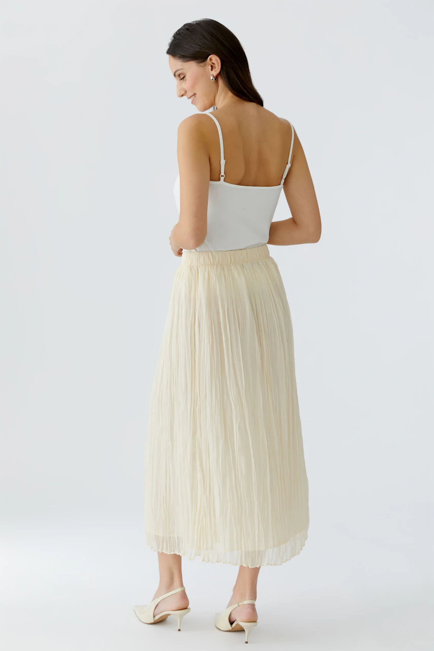 Light pleated skirt: Woman in a flowing cream skirt with a relaxed fit, showcasing a casual style.