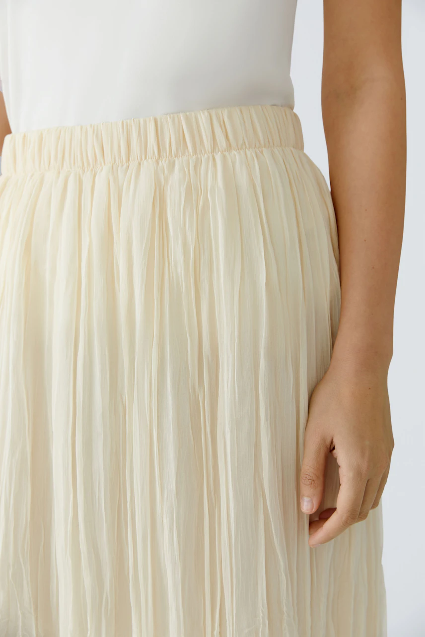 Light pleated skirt: Woman wearing a flowing, cream-colored pleated skirt with an elastic waistband.