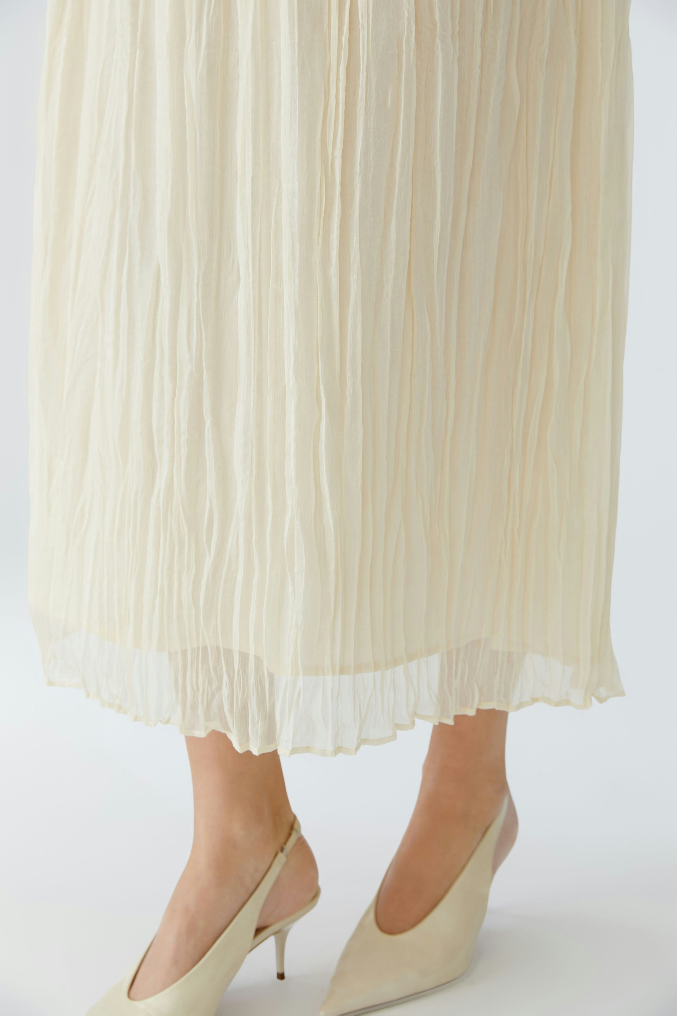 Light pleated skirt: A woman wearing a flowing, cream-colored pleated skirt paired with stylish heels.