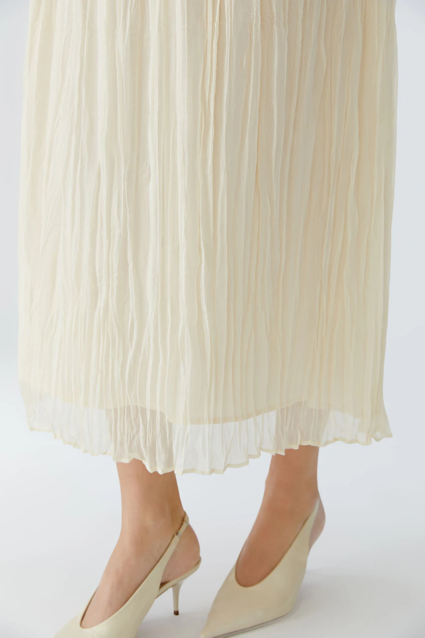 Light pleated skirt: A woman wearing a flowing, cream-colored pleated skirt paired with stylish heels.