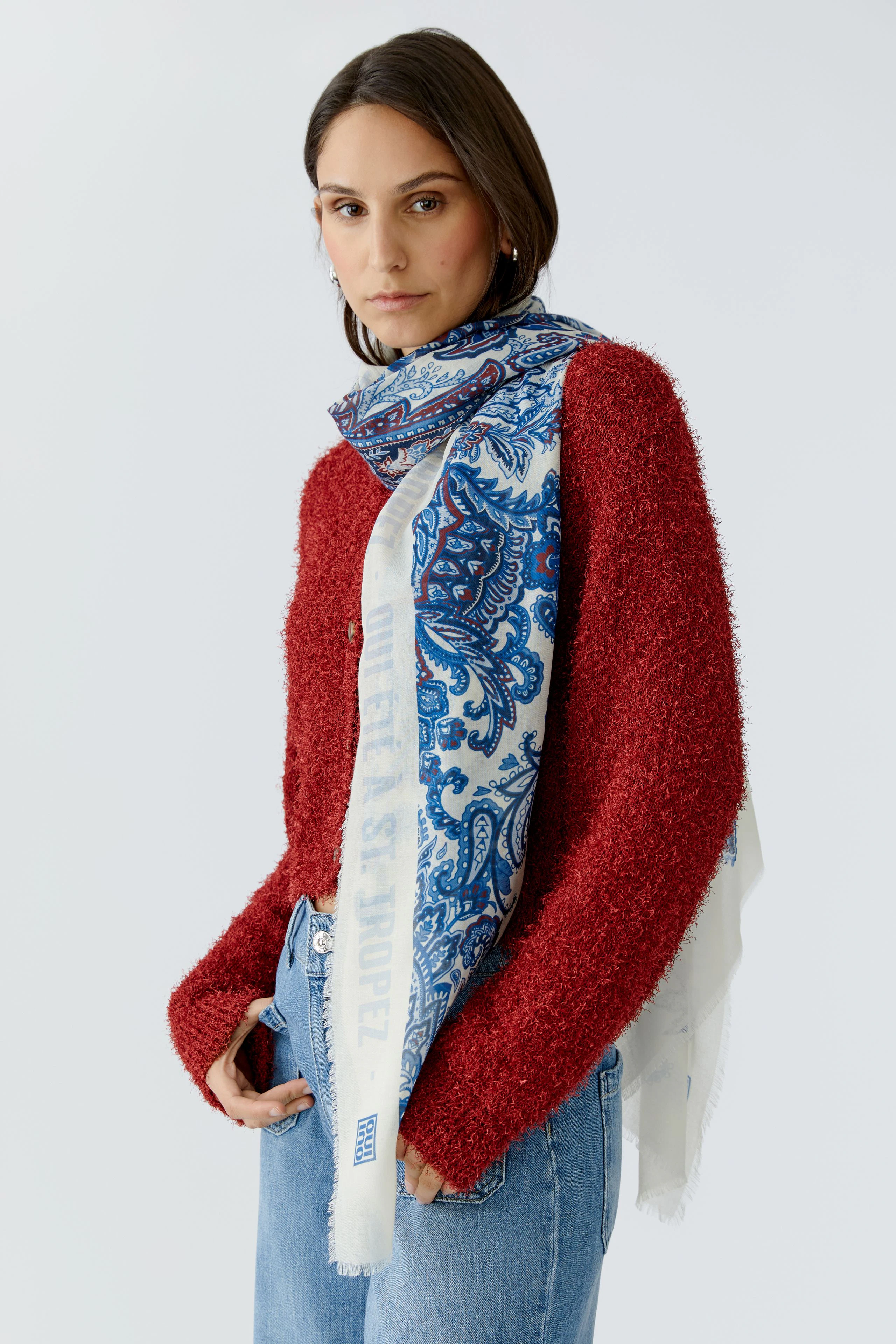 Stylish scarf: Woman wearing a blue patterned scarf over a red sweater, adding a pop of color.