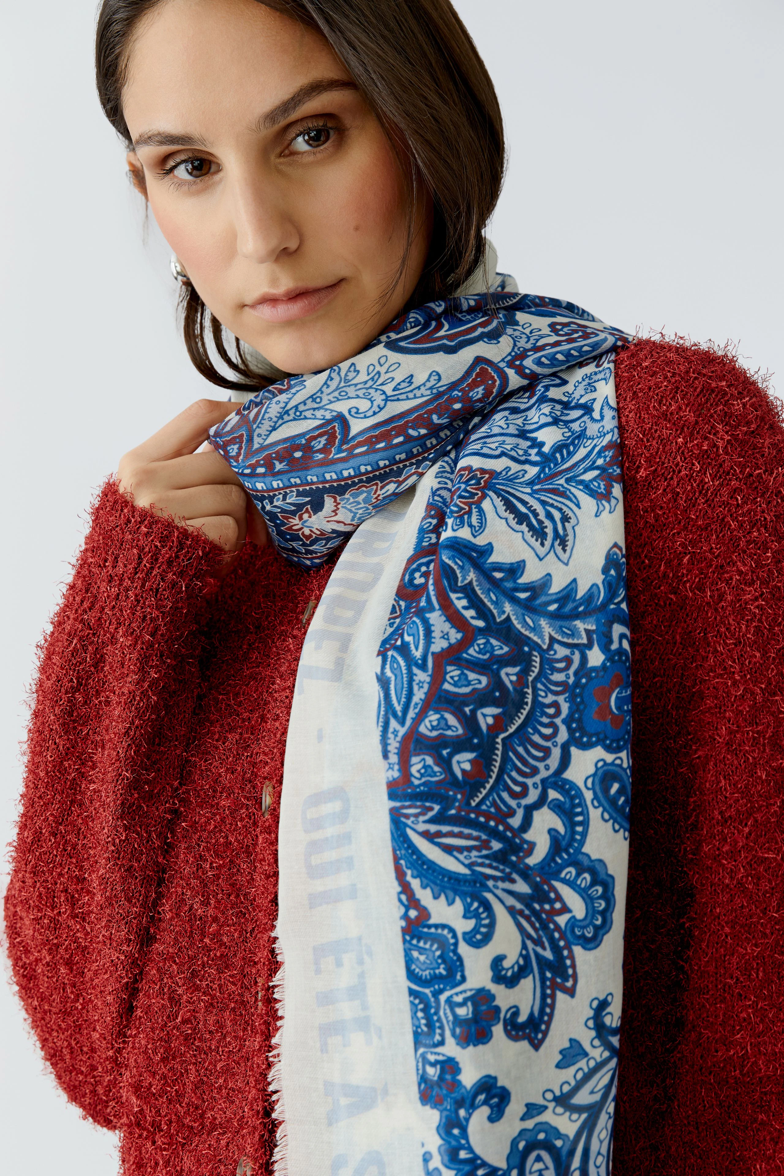 Stylish women's scarf: A woman wearing a patterned scarf with blue and white designs, paired with a cozy red sweater.