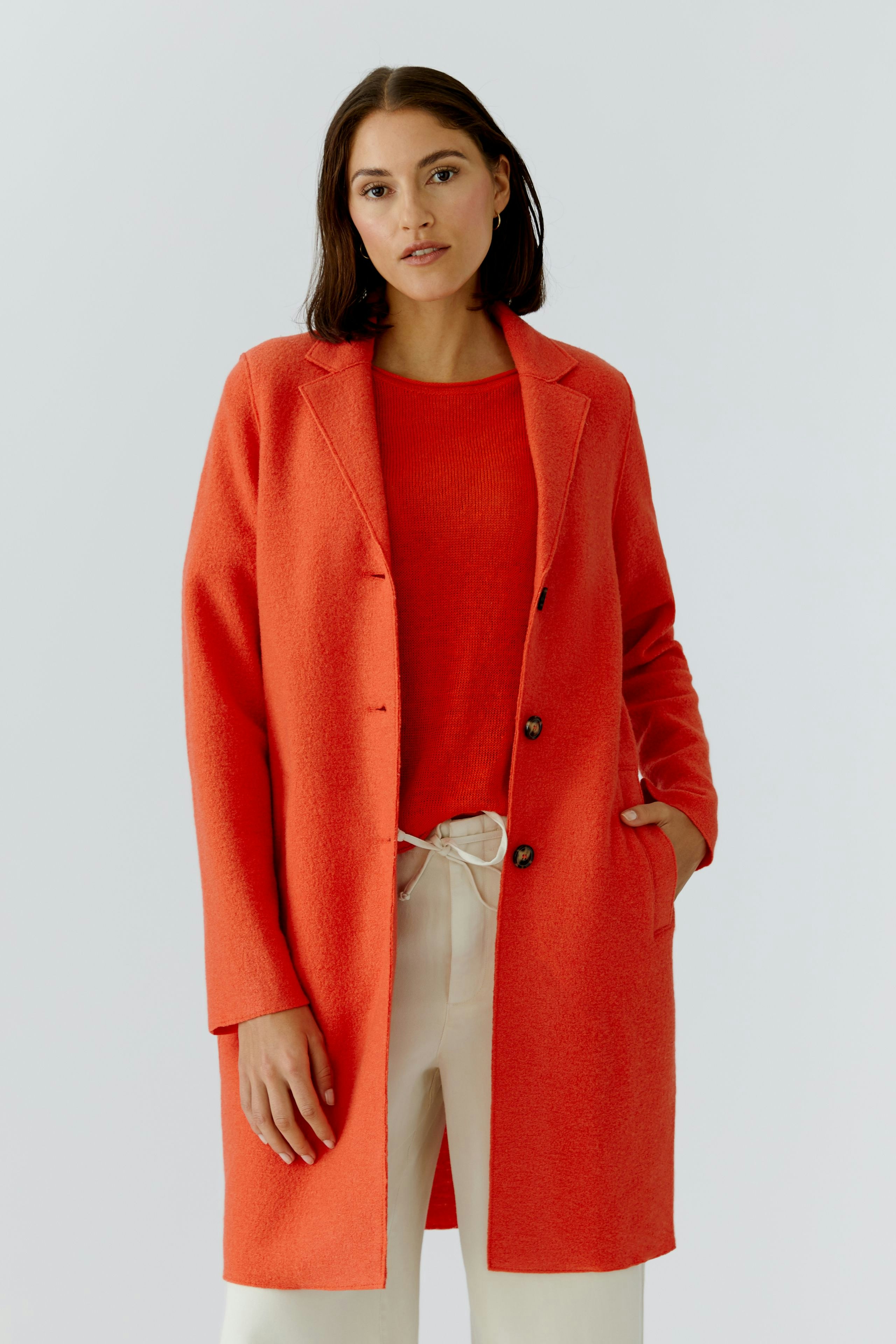 Wollmantel: Frau in rotem Wollmantel mit Knöpfen, kombiniert mit einem roten Oberteil und hellen Hosen.