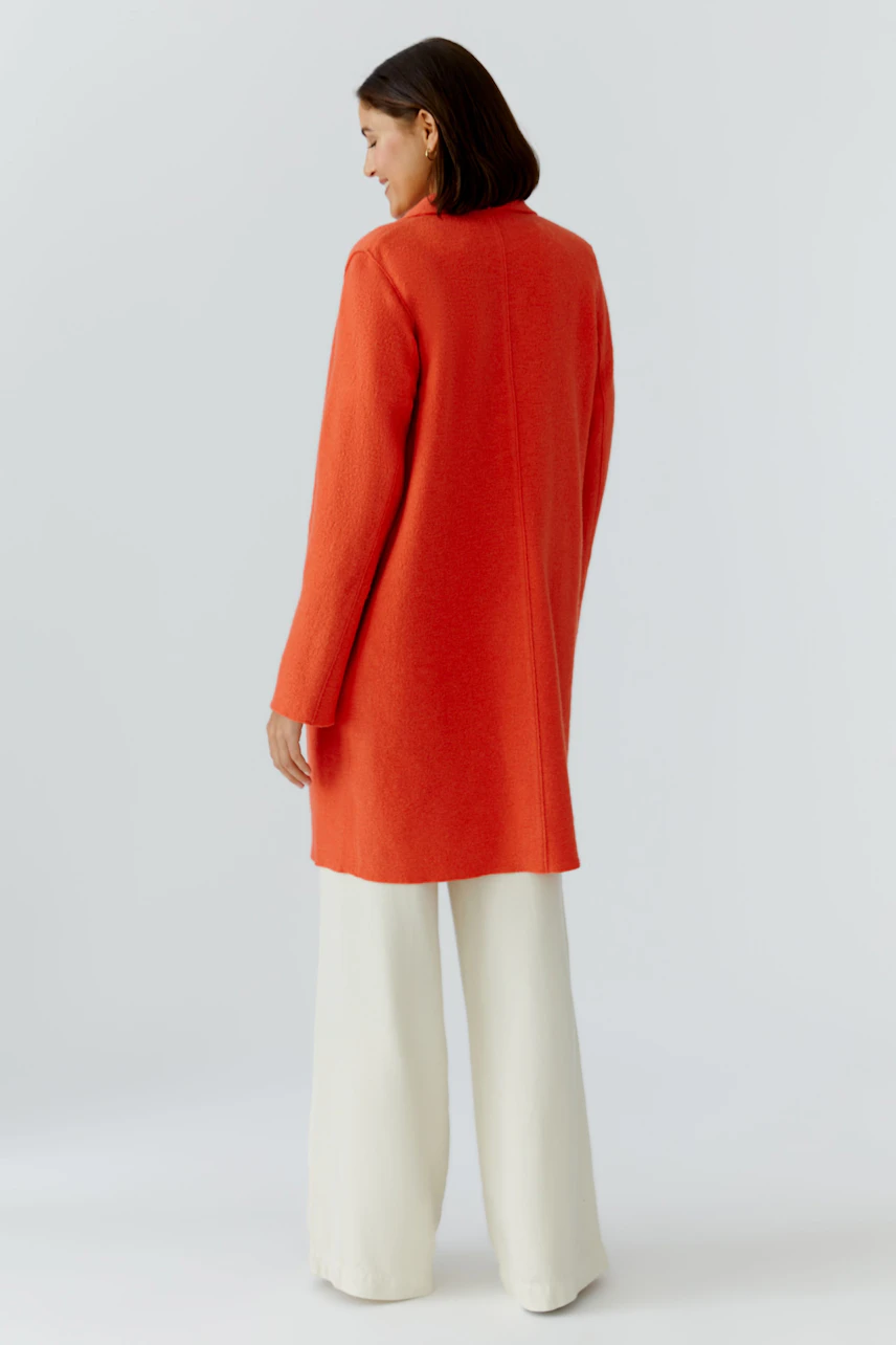 Wollmantel: Frau in orangefarbenem, langem Mantel mit lässigem Schnitt und weichem Material.