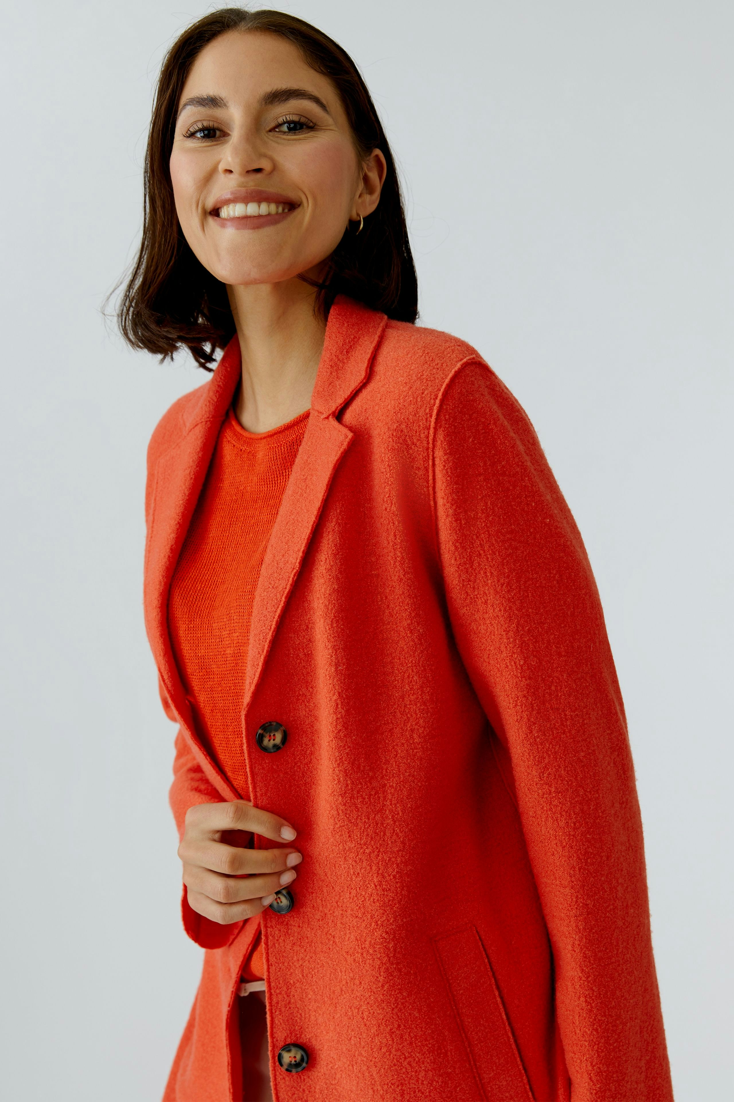 Wollmantel: Frau in leuchtend rotem Wollmantel mit Knöpfen und lässigem Look lächelt freundlich.