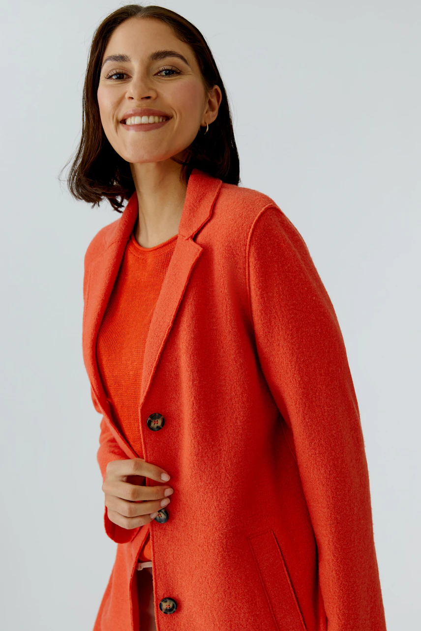 Wollmantel: Frau in leuchtend rotem Wollmantel mit Knöpfen und lässigem Look lächelt freundlich.