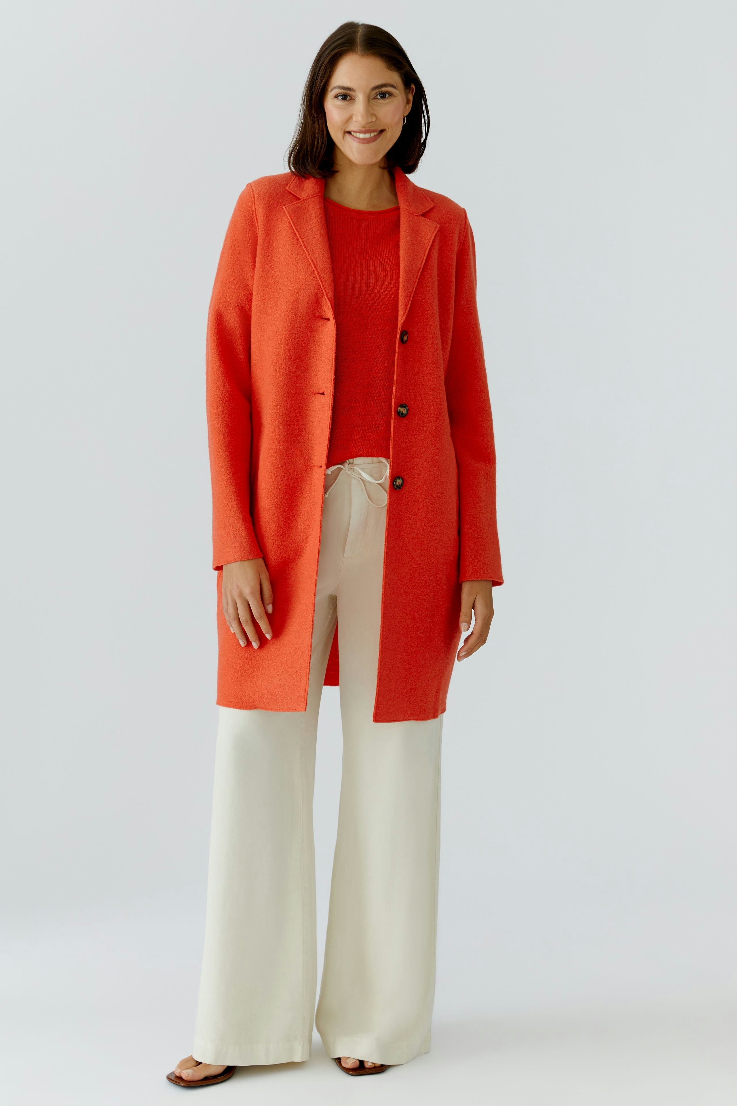 Damen Wollmantel: Frau in rotem Wollmantel mit Knöpfen, kombiniert mit lässigem Oberteil und weiten Hosen.