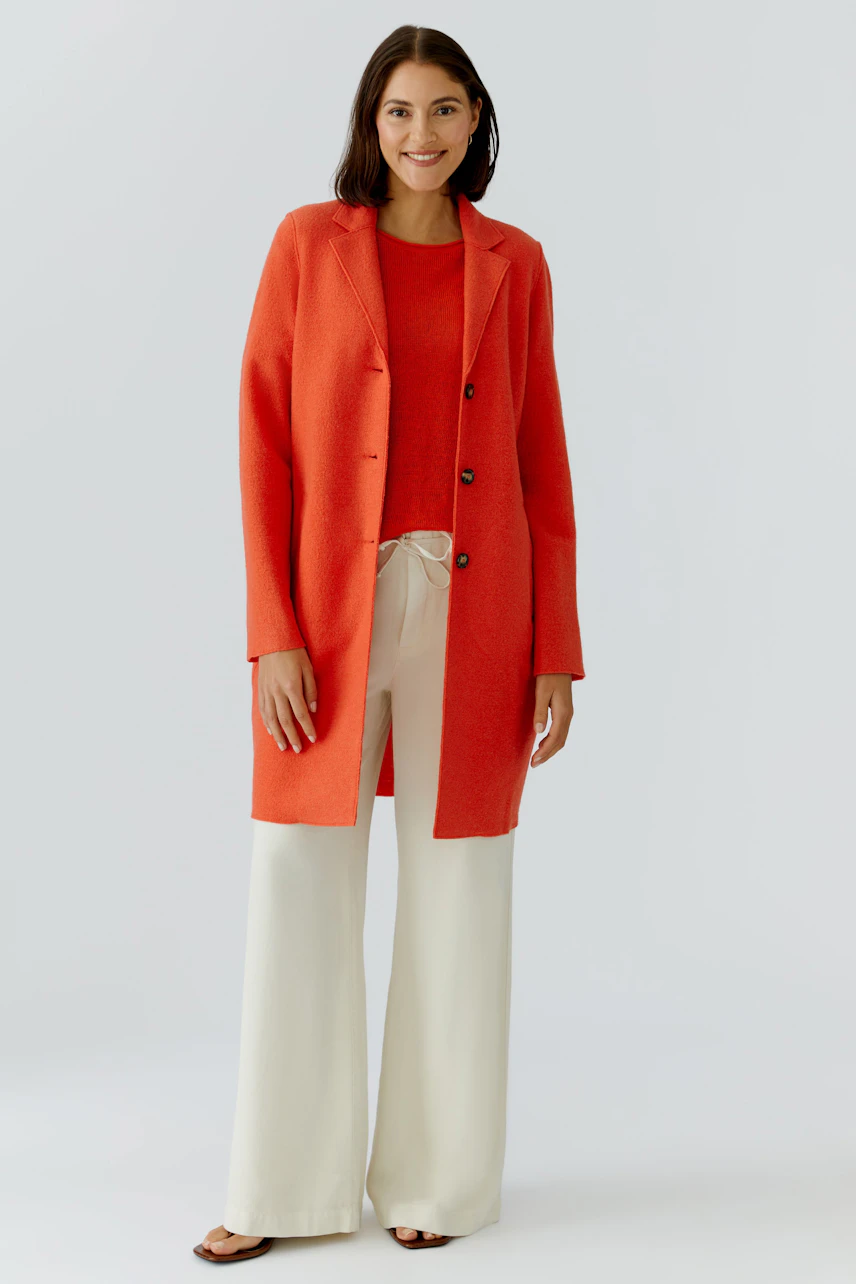 Damen Wollmantel: Frau in rotem Wollmantel mit Knöpfen, kombiniert mit lässigem Oberteil und weiten Hosen.