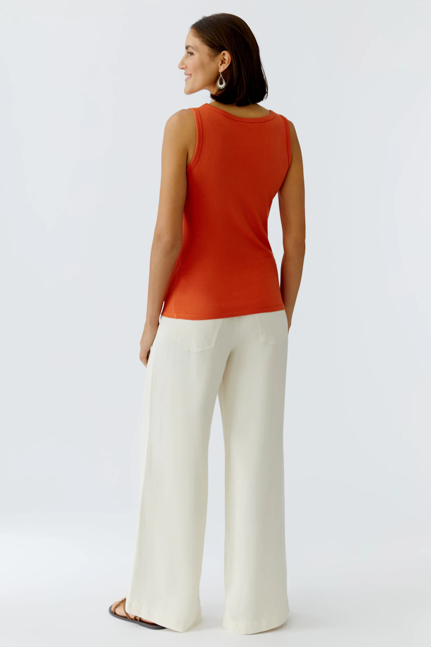 Casual women's top: A woman in a fitted orange tank top paired with light, wide trousers.