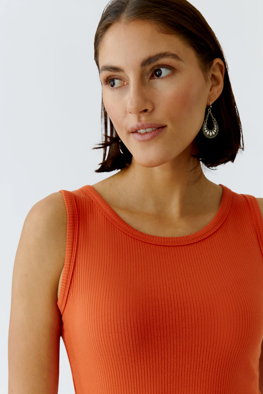 Casual women's top: Young woman in a vibrant orange ribbed top, showcasing a relaxed style.