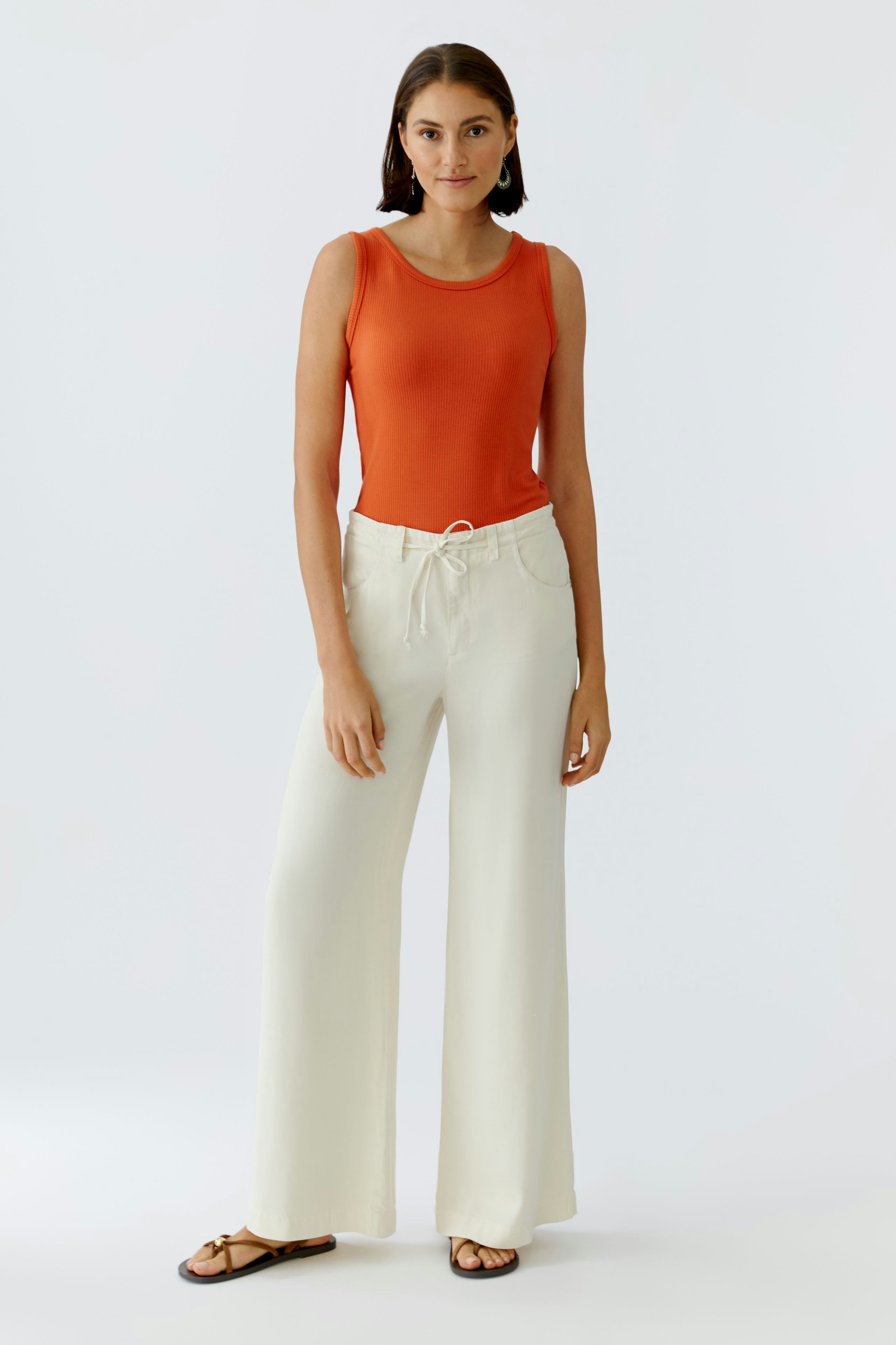 Casual women's top: A woman in an orange tank top paired with light wide-leg pants stands confidently.
