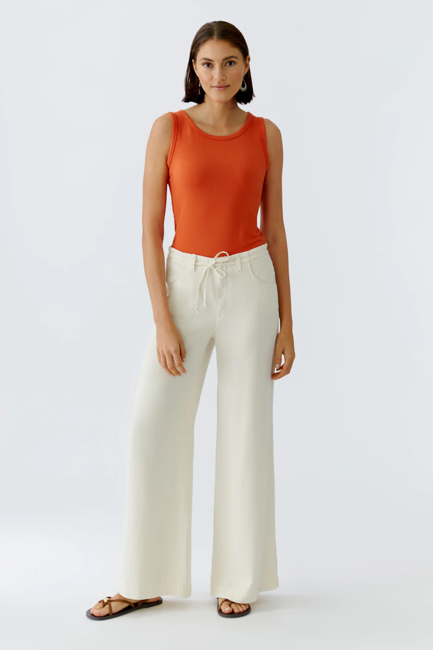 Casual women's top: A woman in an orange tank top paired with light wide-leg pants stands confidently.