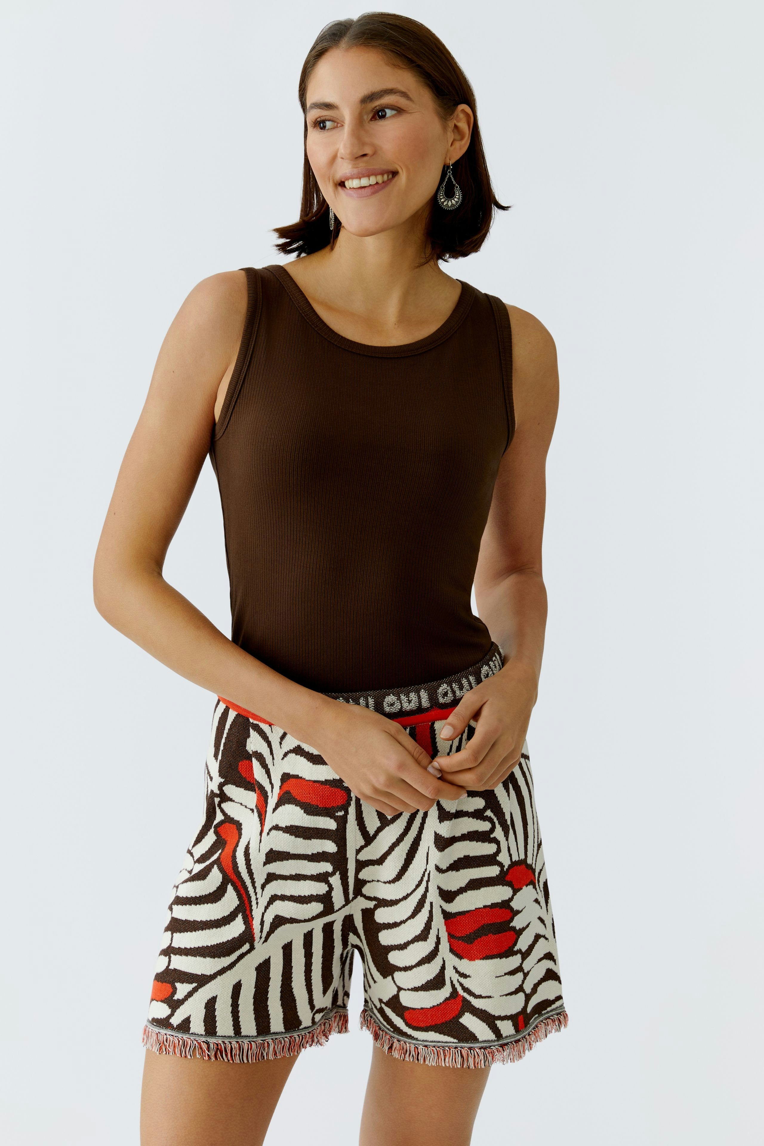 Casual women's top: A woman in a brown tank top paired with patterned shorts, smiling confidently.