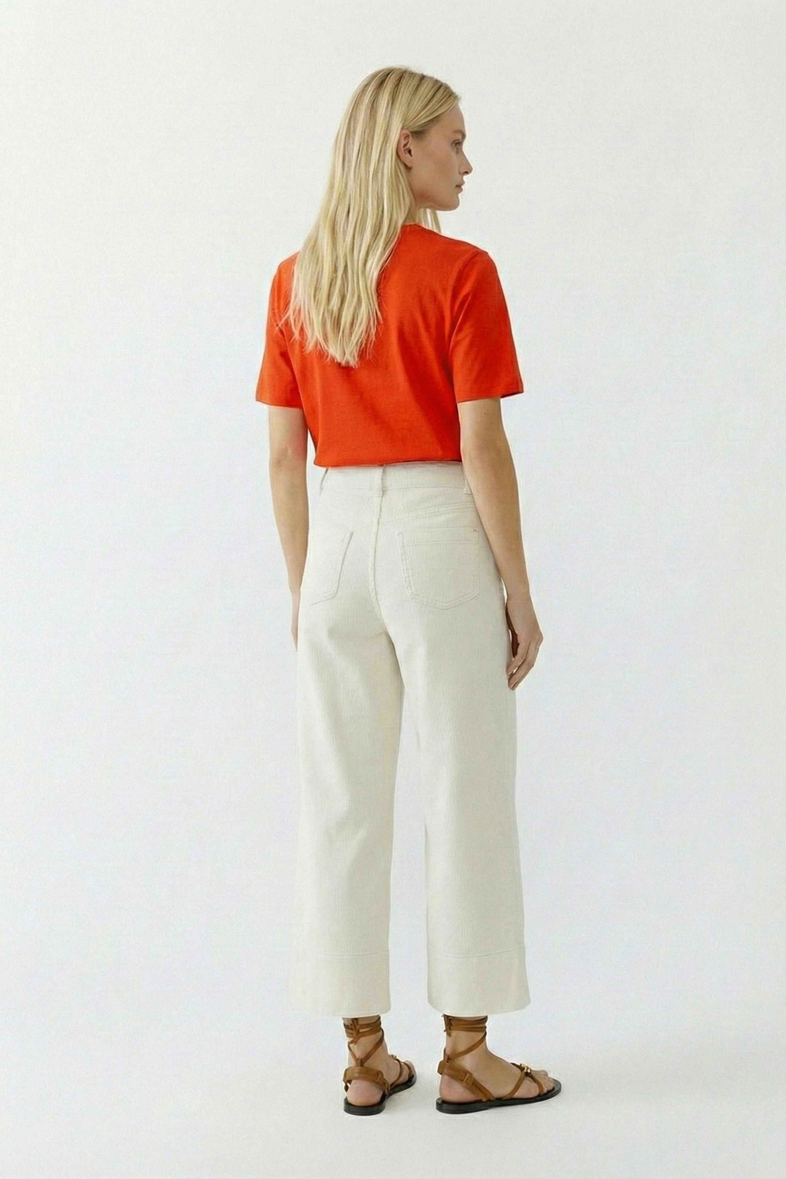 Casual women's T-shirt: Young woman in a bright orange tee paired with light trousers, showcasing a relaxed style.