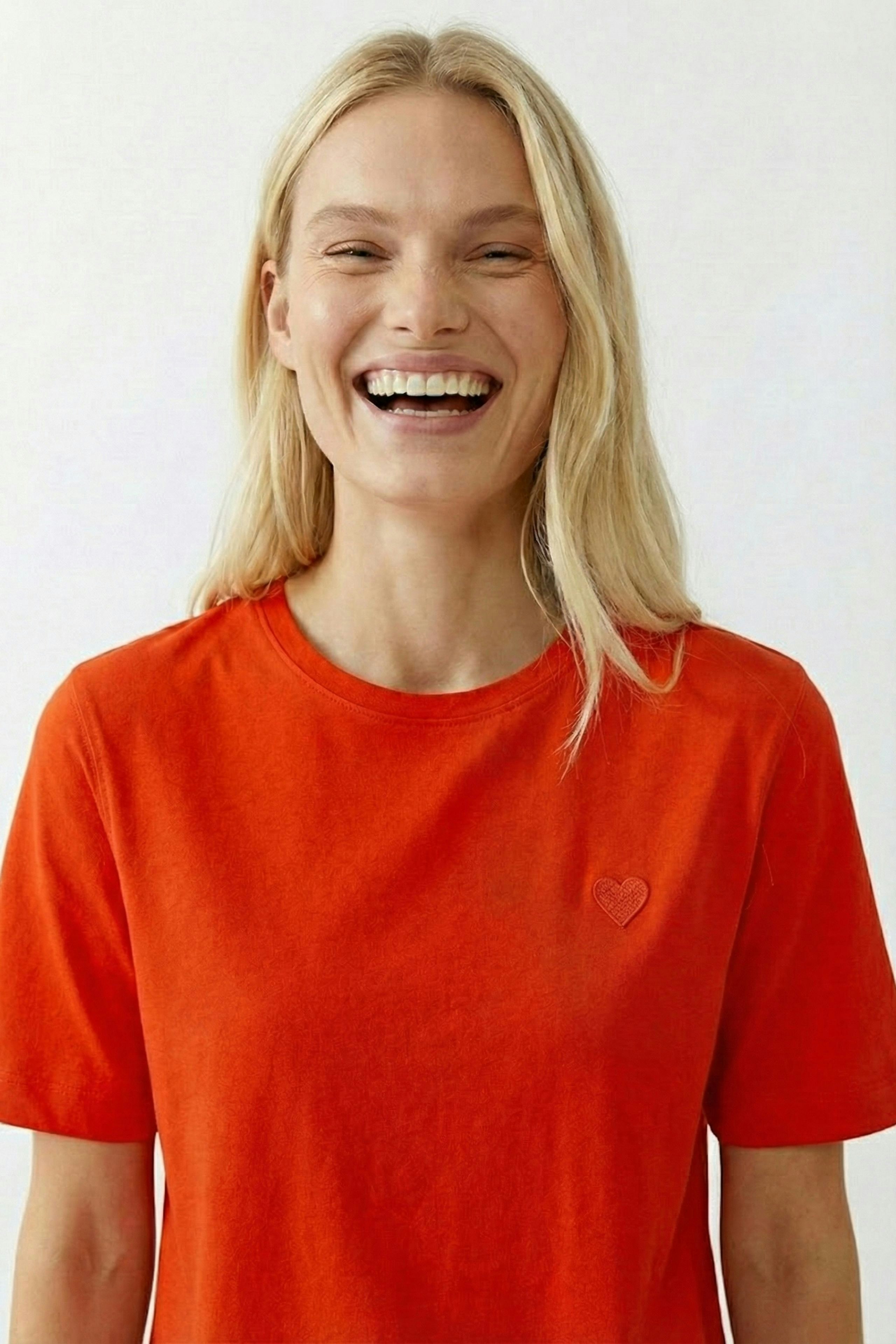 Casual women's T-shirt: Smiling woman in a bright orange tee with a heart detail.