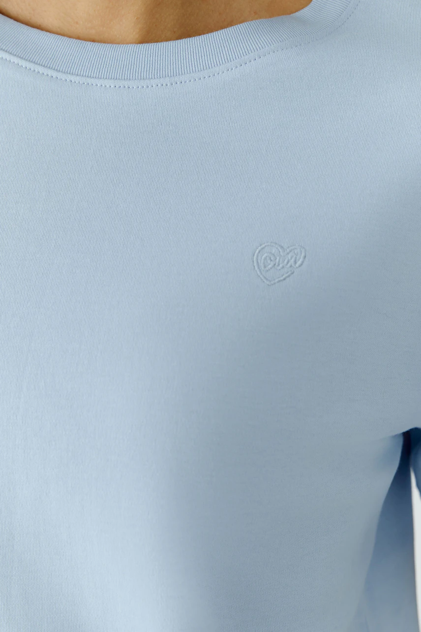 Bequemes Damen-T-Shirt: Frau trägt ein hellblaues T-Shirt mit dezentem Logo auf der Brust.