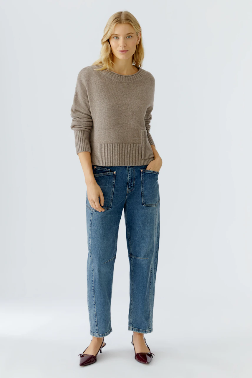 Casual women's pullover: A woman in a light brown pullover with a relaxed fit and pocket, paired with jeans.