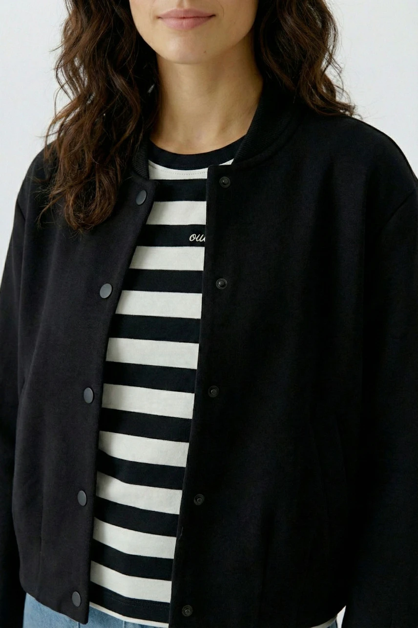 Damen-Bomberjacke: Frau in schwarzer Jacke über gestreiftem Shirt, lässiger Look.