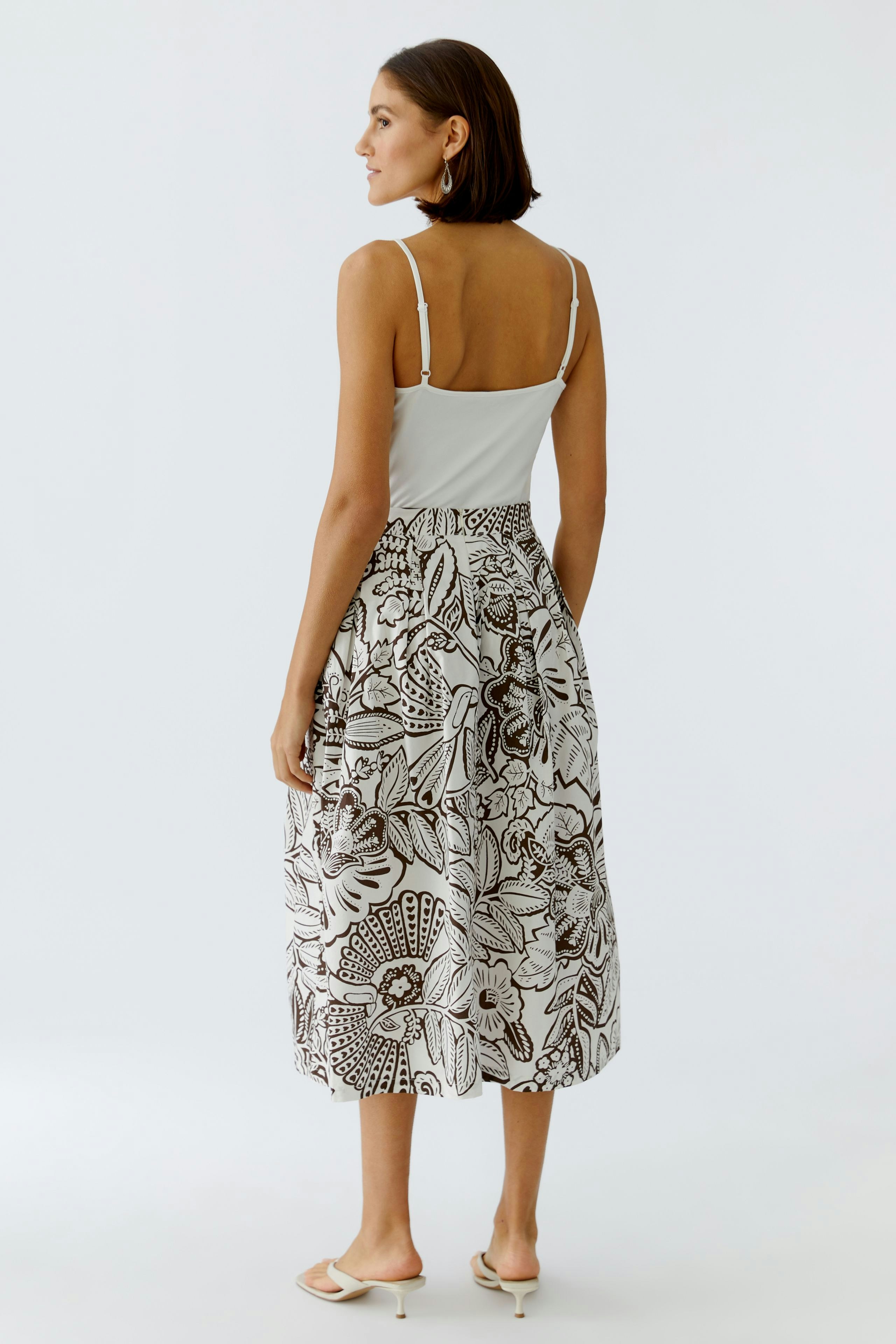 Faltenrock: Frau trägt einen gemusterten Faltenrock mit weitem Schnitt und Trägertop.