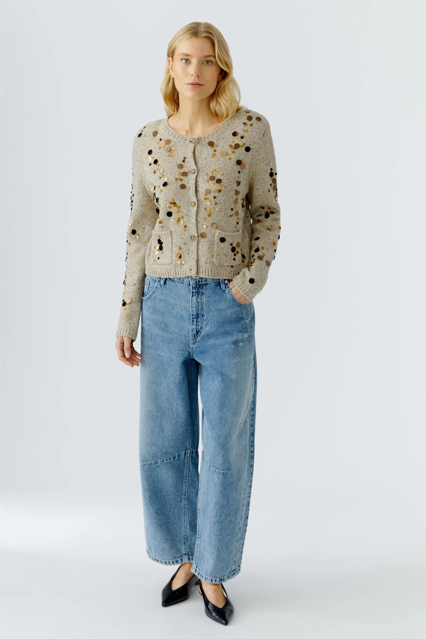 Casual women's cardigan: A woman in a beige cardigan with colorful details and relaxed-fit jeans.