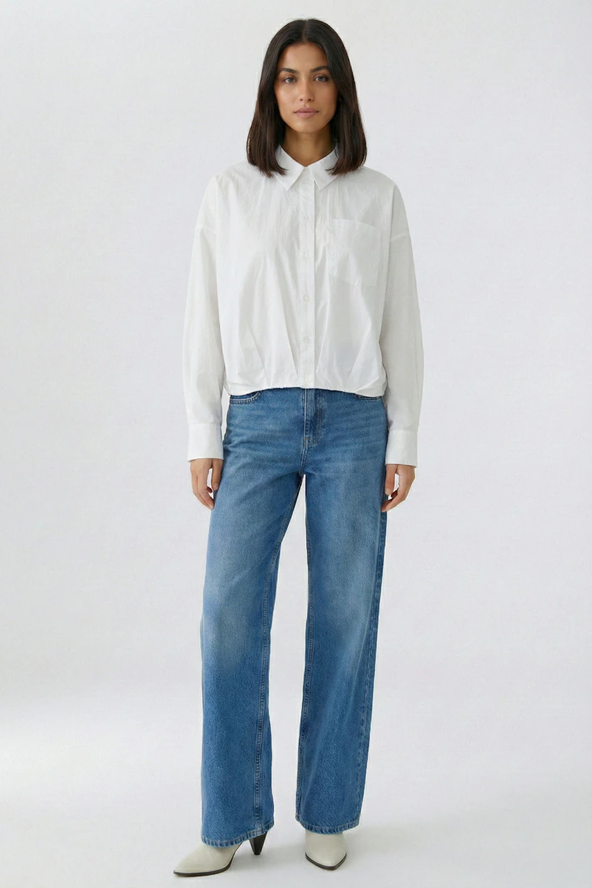 Weiße Damen-Bluse: Frau in lockerer Bluse und blauer Jeans, schlicht und modern.