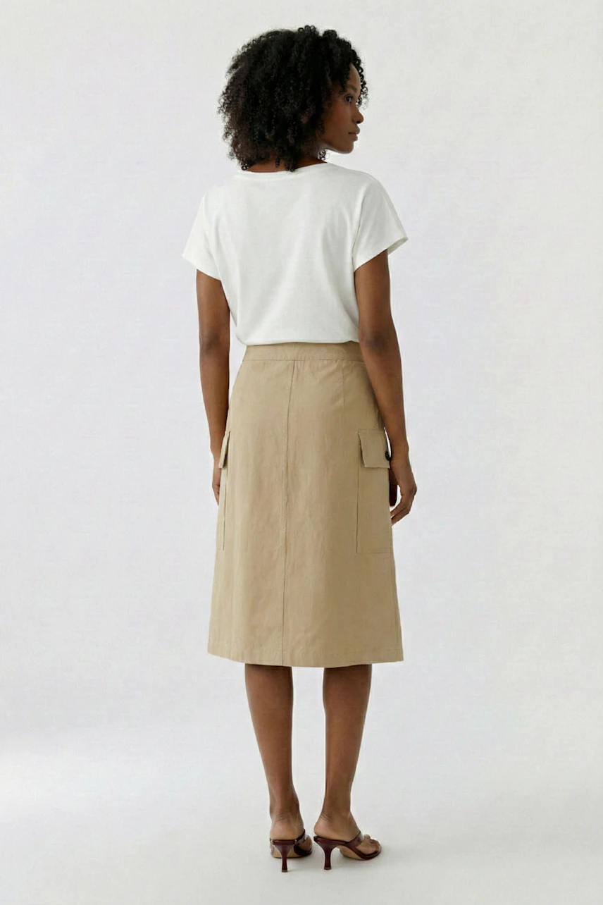 A-Linien-Rock: Frau im beigen Rock mit Taschen, kombiniert mit weißem T-Shirt, von hinten gesehen.