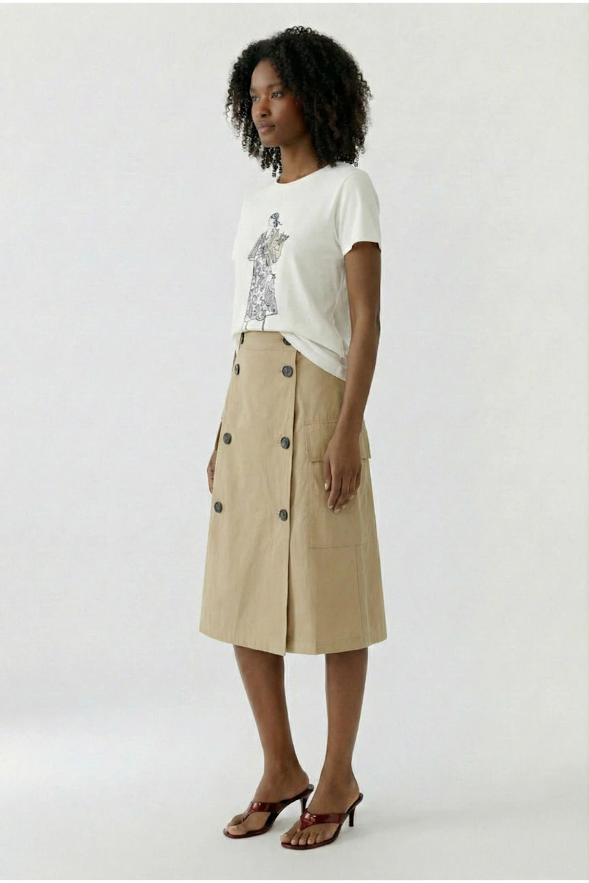 A-Linien-Rock: Frau im beigen Rock mit Knopfleiste und weißem T-Shirt, seitlich stehend.