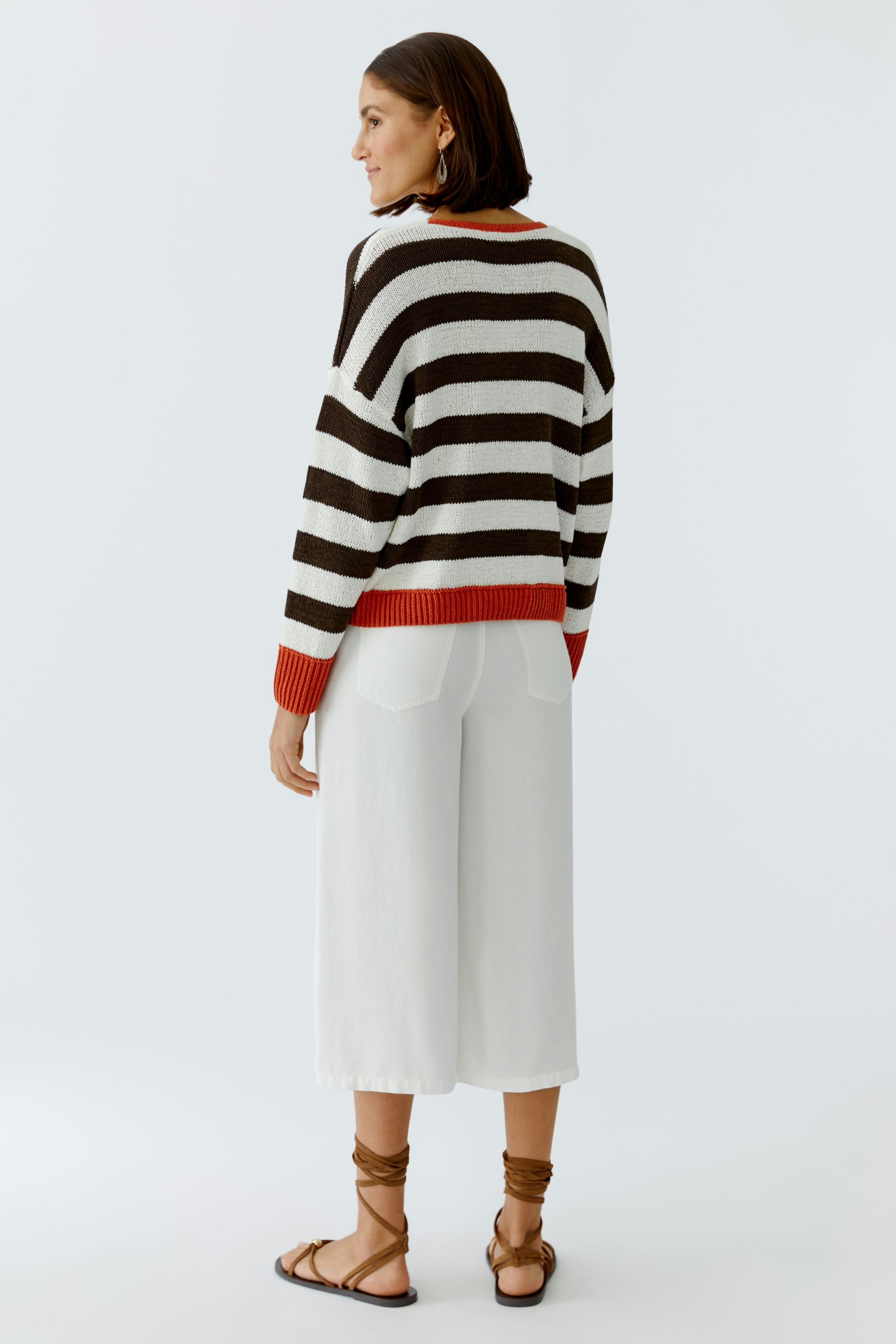 Damen-Pullover: Frau mit gestreiftem Pullover in Braun und Weiß, lässig kombiniert mit weißen Hosen.