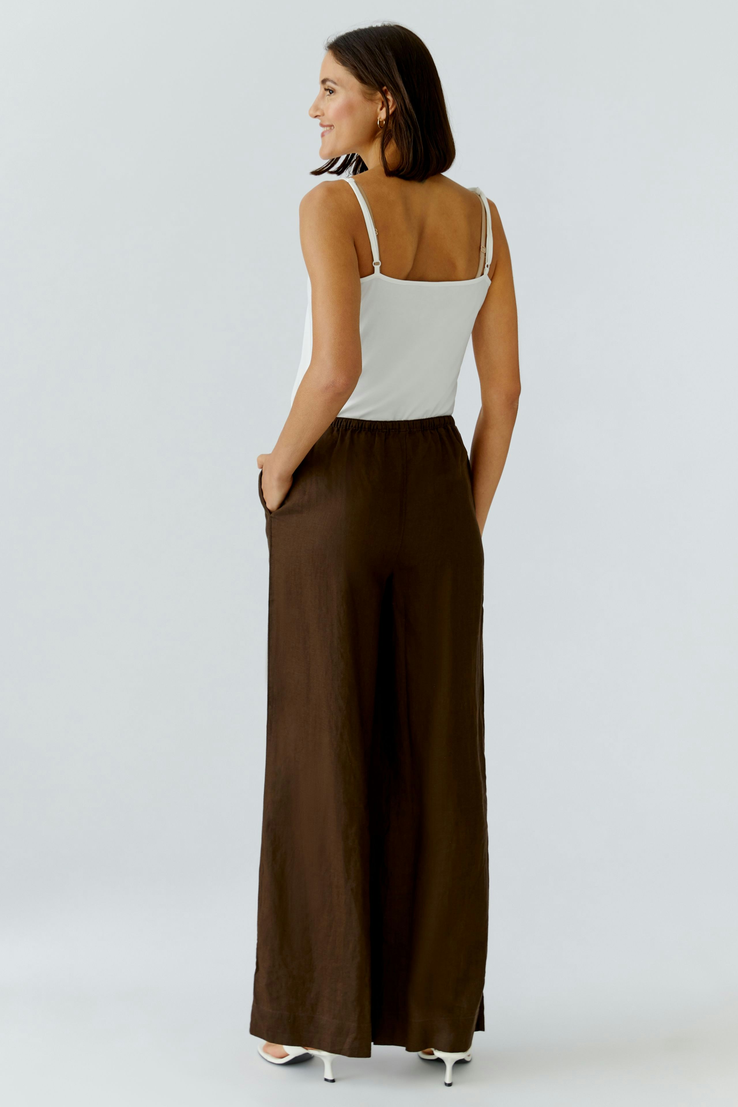 Bequeme Marlenehose: Frau in braunen, weiten Hosen mit elastischem Bund und seitlichen Taschen.