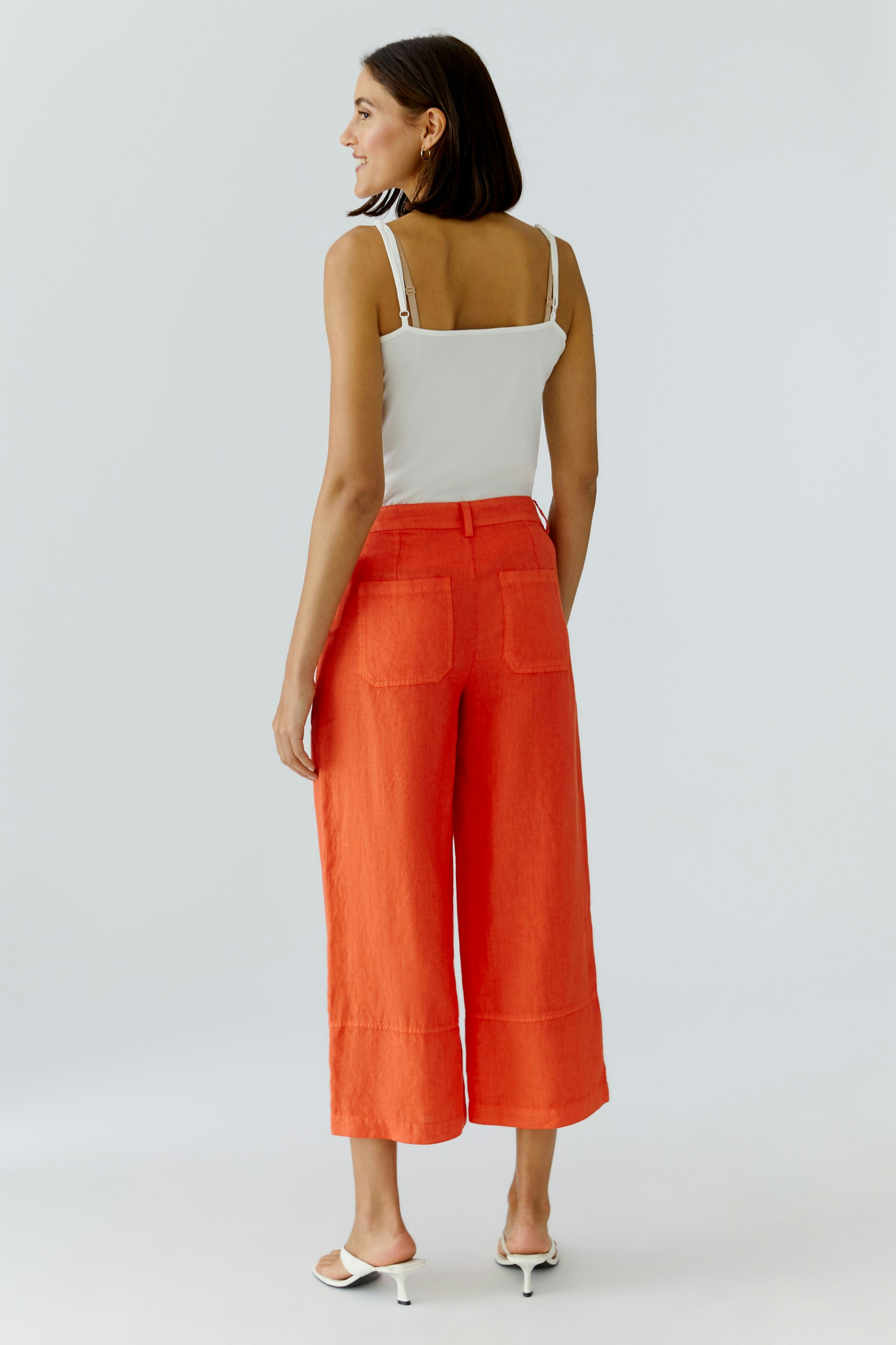 Bequeme Damen-Hose: Frau trägt eine lässige, orangefarbene Hose mit weitem Bein und praktischen Taschen.