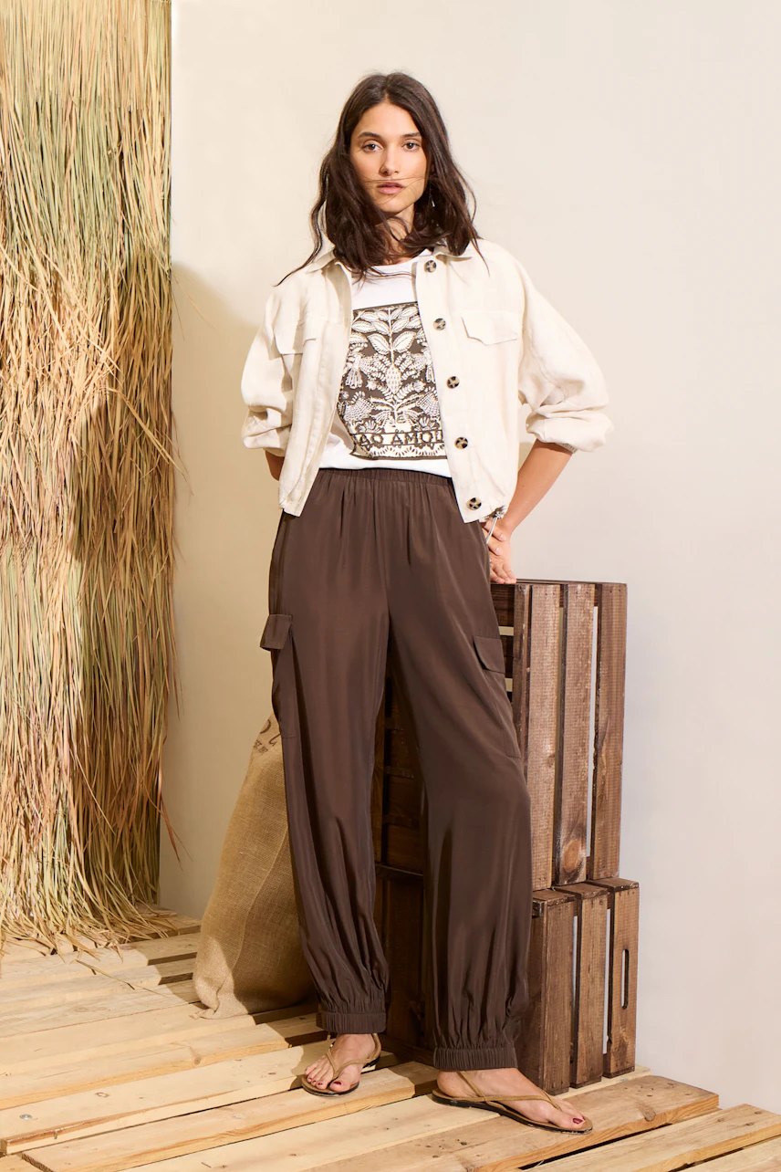 Casual cargo pants: Woman in brown cargo pants with a white jacket and graphic tee, standing confidently.