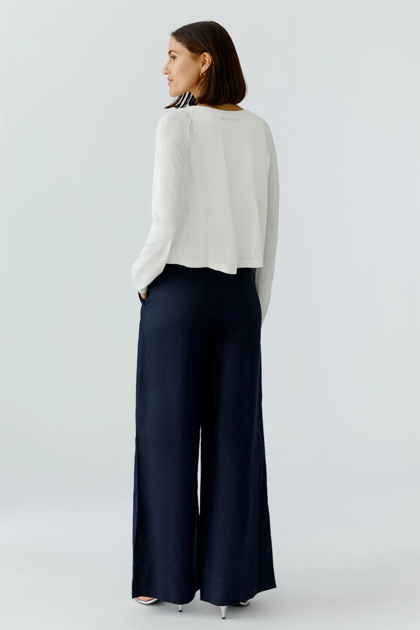 Casual women's cardigan: A woman in a white cardigan paired with wide-leg navy pants, showcasing a relaxed style.