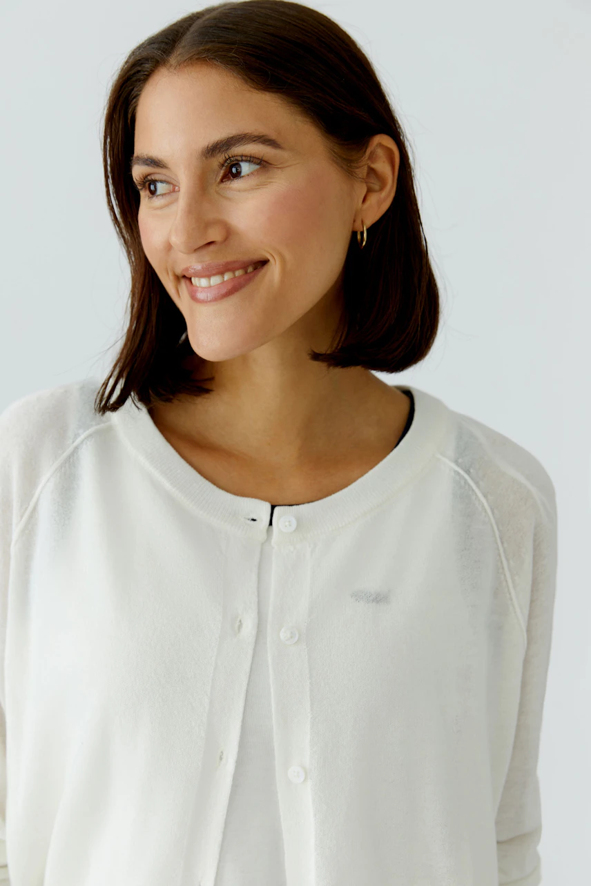Casual women's cardigan: A woman smiles while wearing a light white cardigan with buttons.