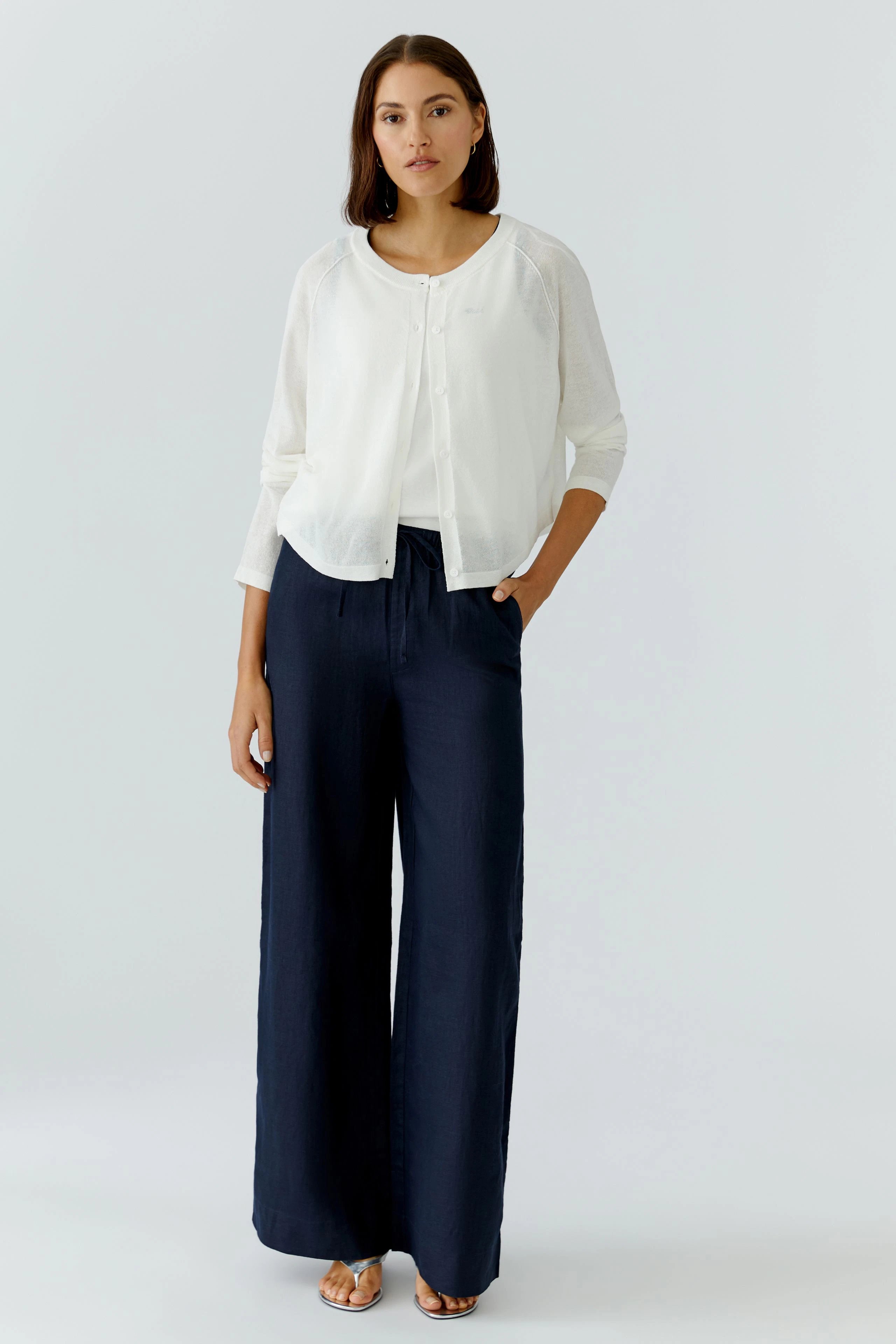 Damen-Strickjacke: Frau in weißer Strickjacke mit lässigem Schnitt und weiten, blauen Hosen.