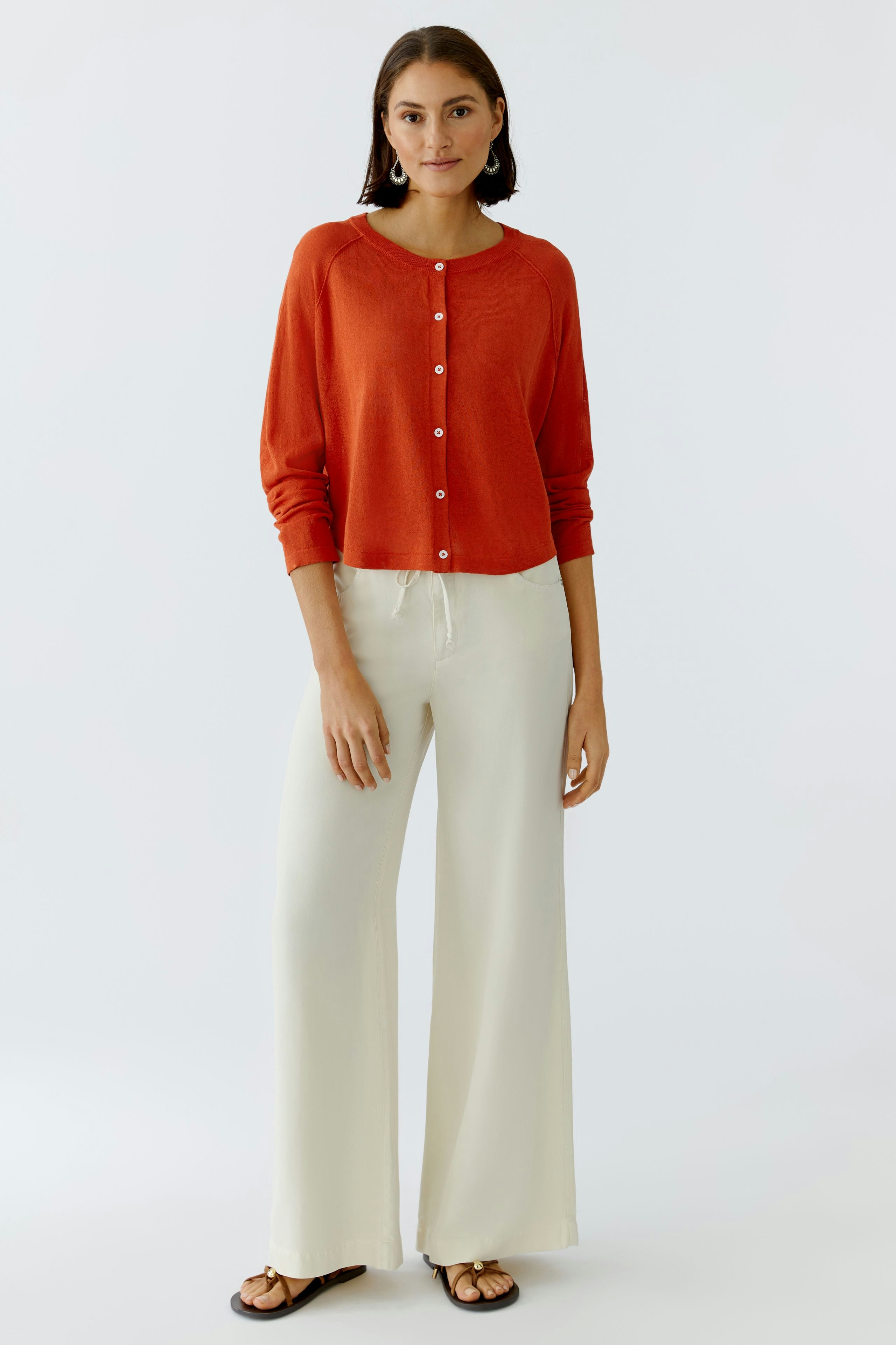 Damen-Strickjacke in leuchtendem Rot, lässig kombiniert mit hellen, weiten Hosen.