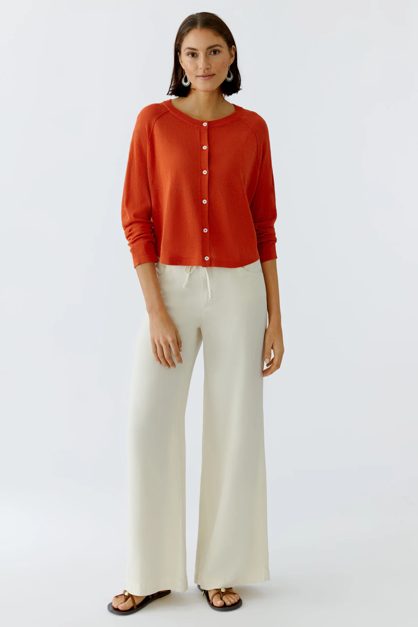 Damen-Strickjacke in leuchtendem Rot, lässig kombiniert mit hellen, weiten Hosen.