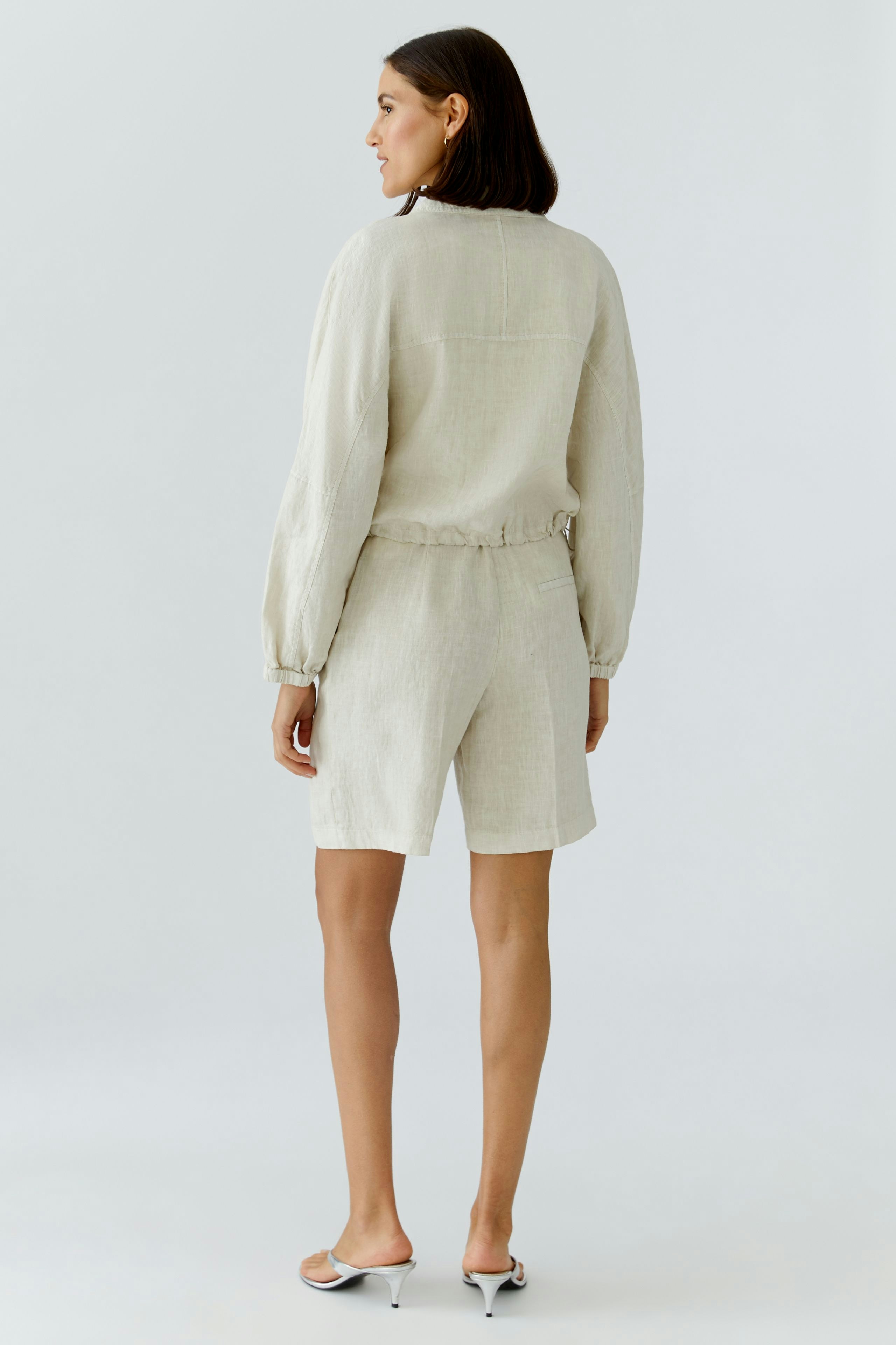 Bequemer Blouson: Frau in hellbeiger Jacke mit elastischem Bund und lässigen Shorts, von hinten zu sehen.