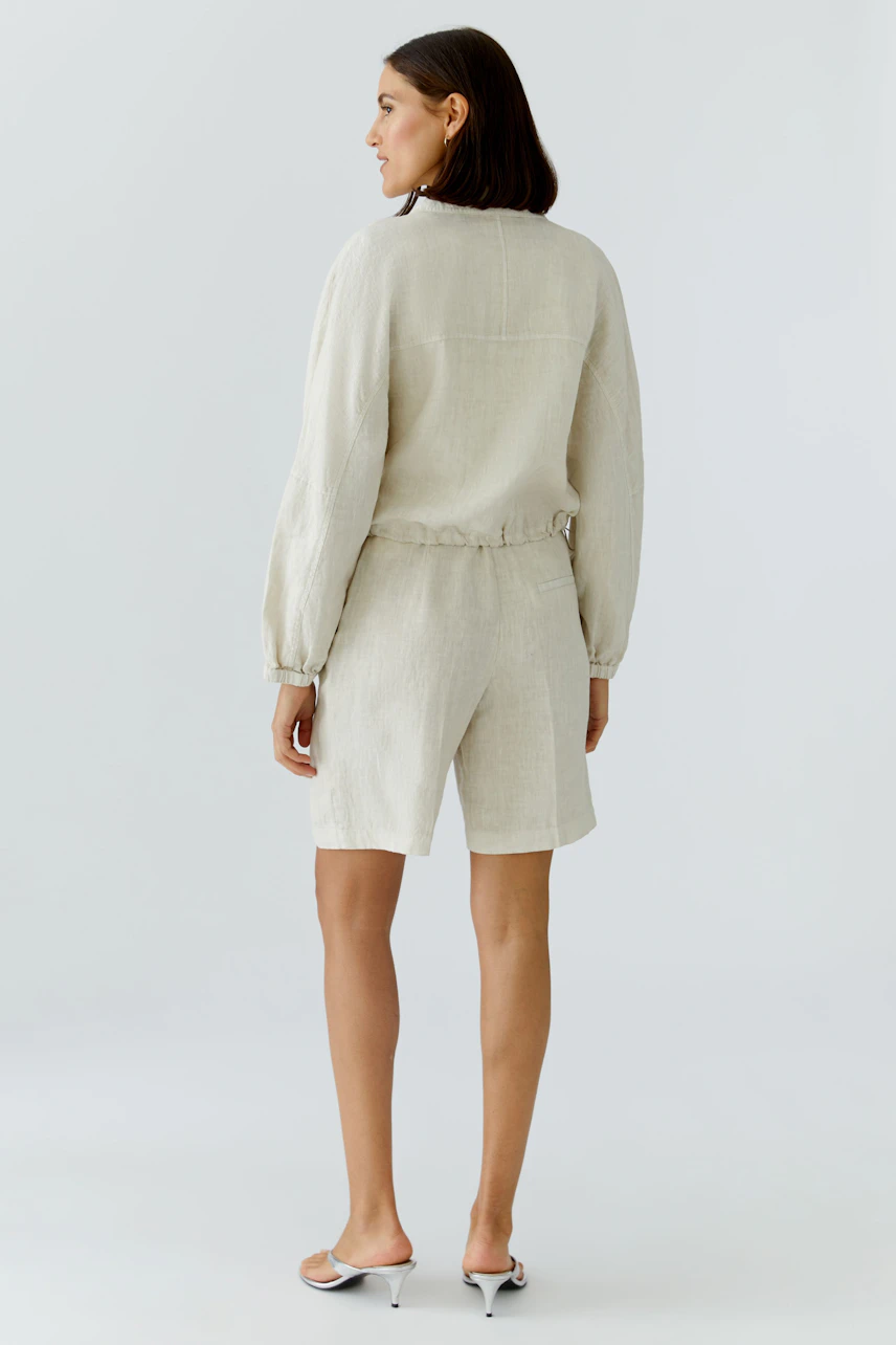 Bequemer Blouson: Frau in hellbeiger Jacke mit elastischem Bund und lässigen Shorts, von hinten zu sehen.