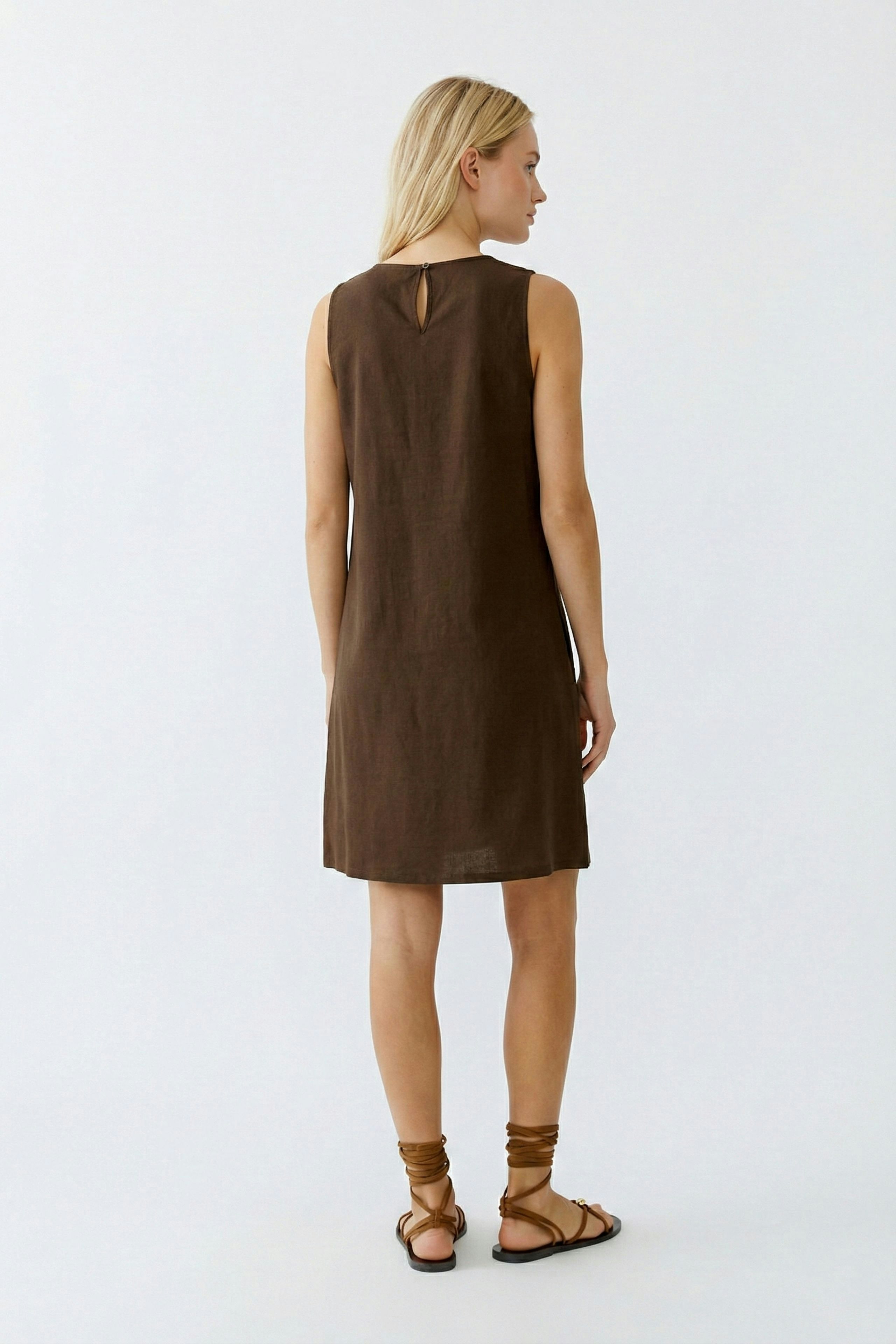 A-Linien-Kleid: Frau trägt ein braunes, ärmelloses Kleid mit Rückenschlitz und Sandalen.