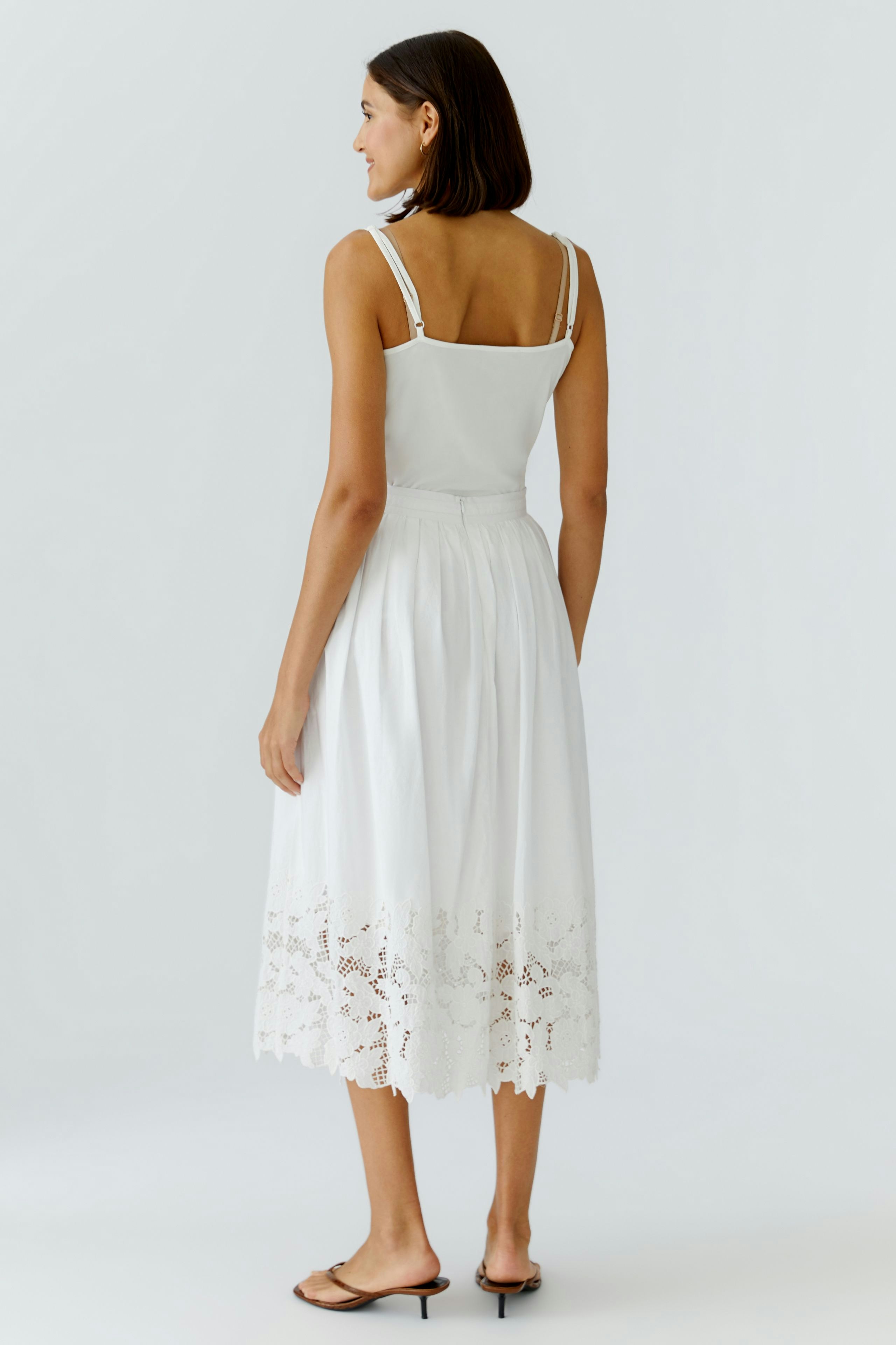 White pleated skirt: Woman in a white skirt with lace hem, showcasing a relaxed summer style.