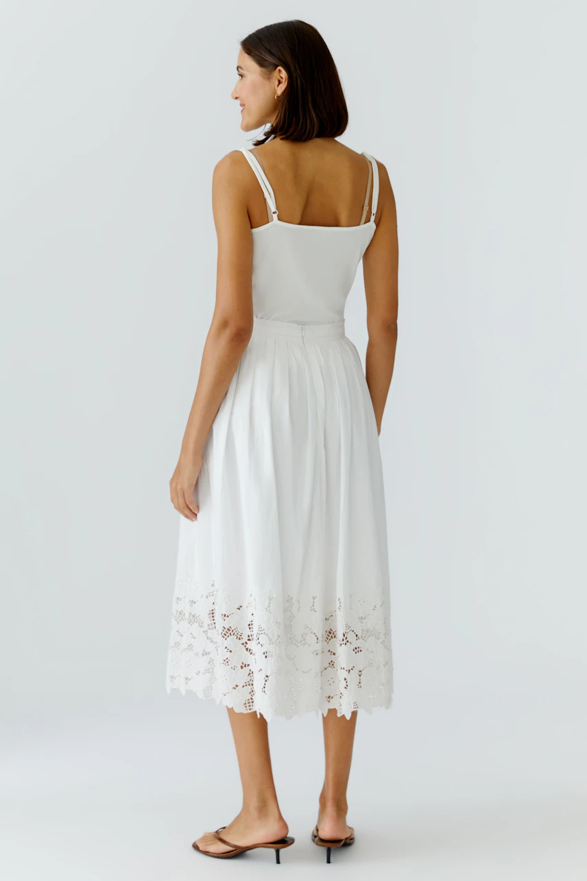 White pleated skirt: Woman in a white skirt with lace hem, showcasing a relaxed summer style.