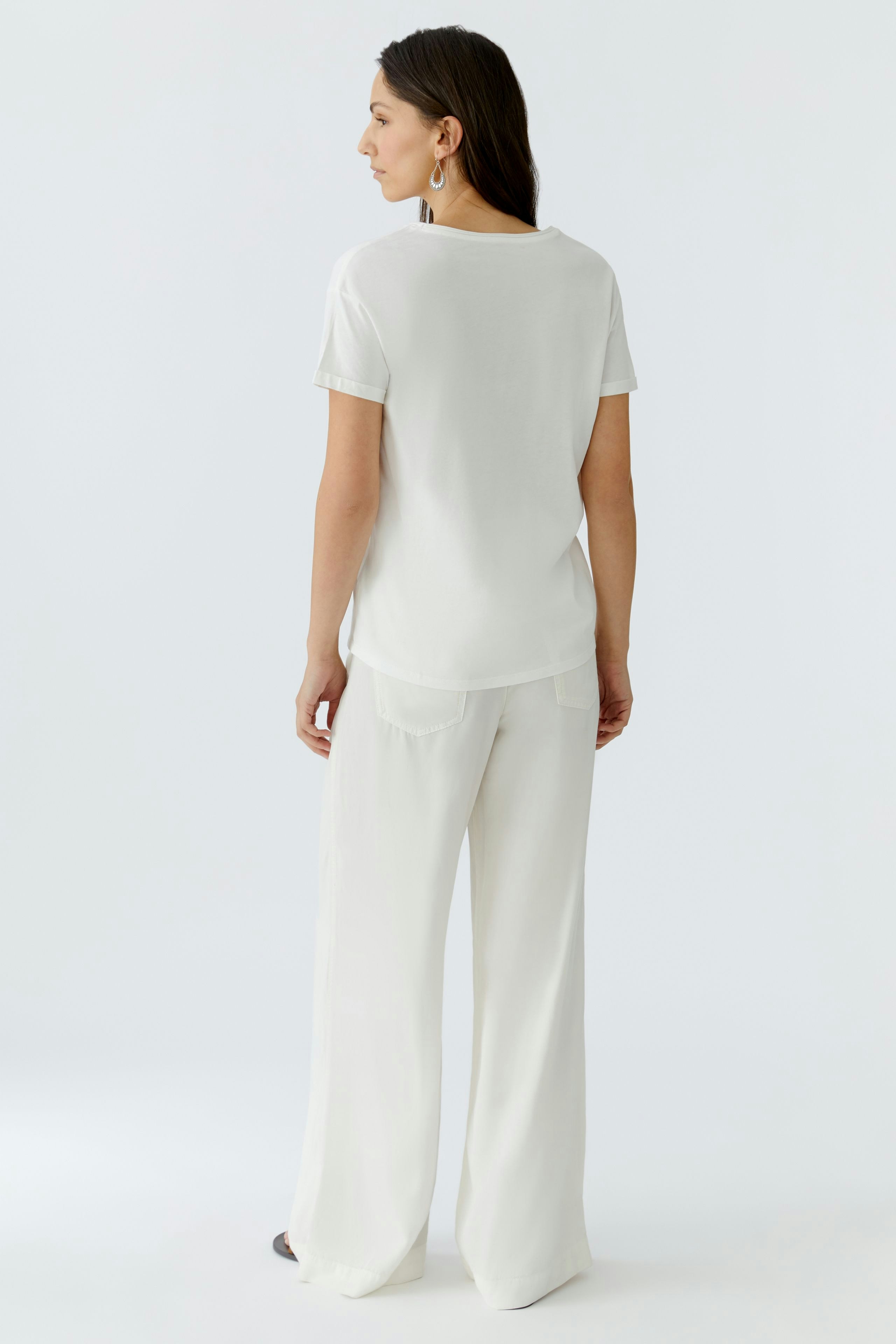 Damen-T-Shirt: Frau trägt ein schlichtes, weißes T-Shirt mit kurzen Ärmeln und lässiger Passform.