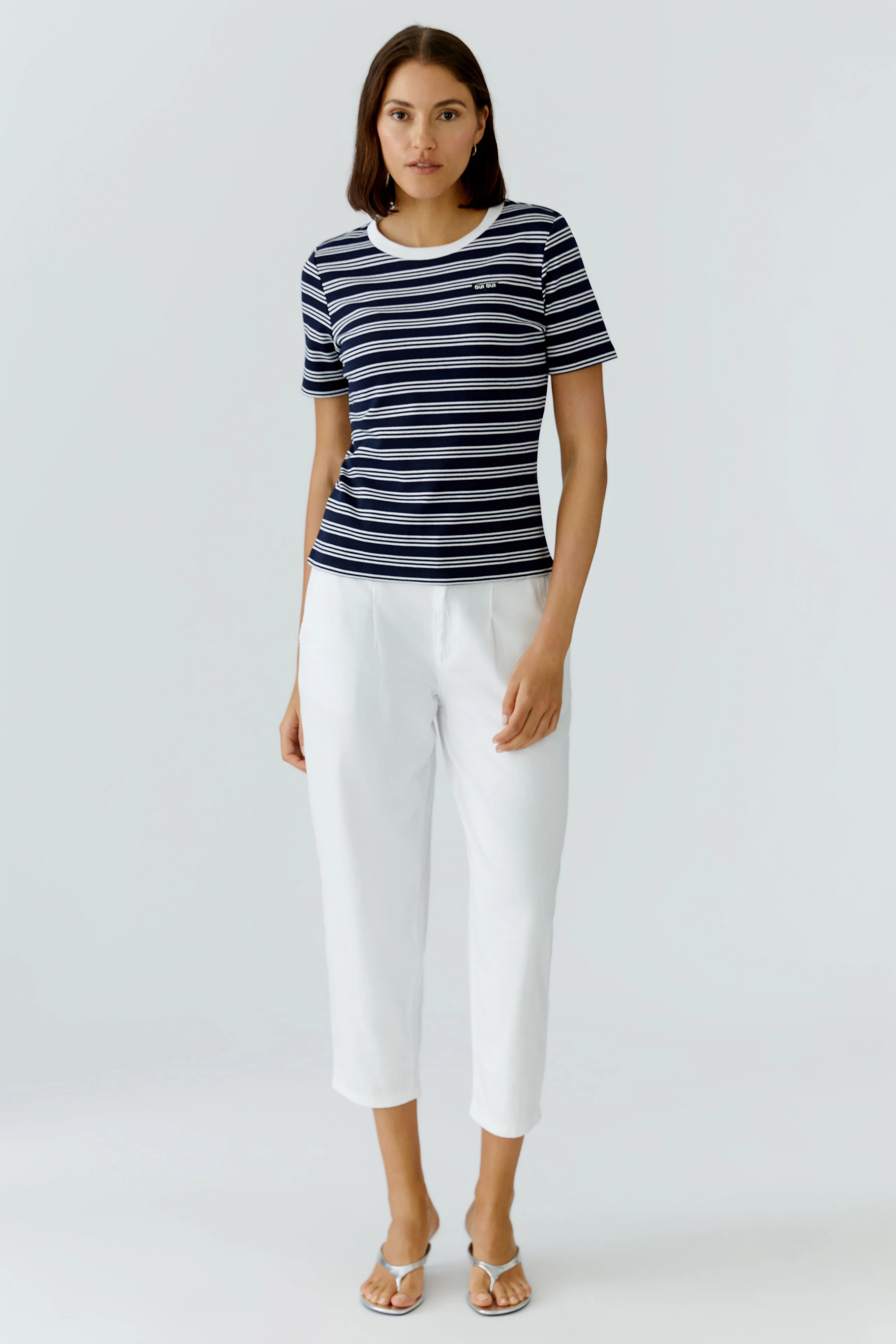 Casual women's T-shirt: Young woman in a navy striped tee paired with white pants, standing confidently.