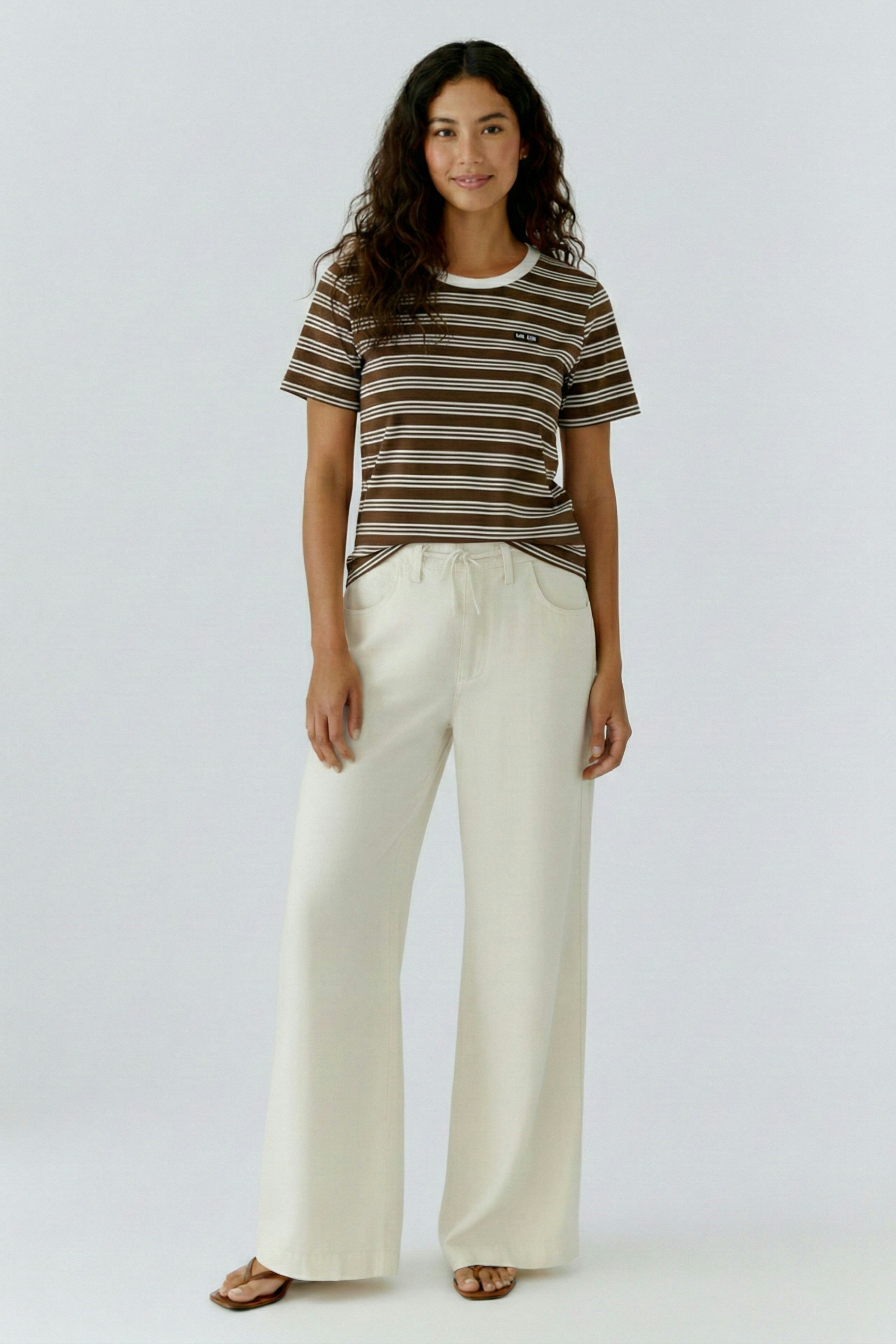 Bequemes Damen-T-Shirt: Frau trägt ein gestreiftes T-Shirt in Braun und Beige, kombiniert mit hellen, weiten Hosen.