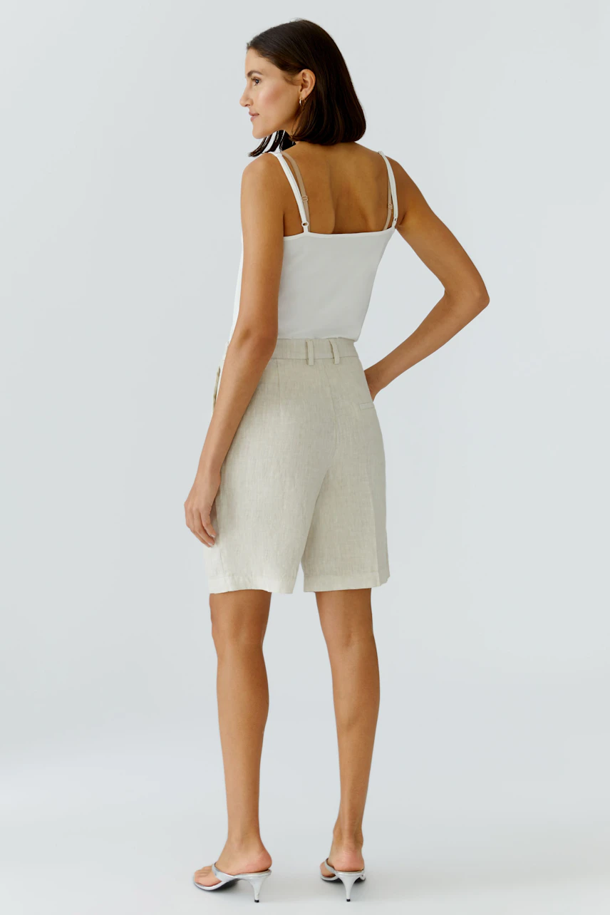 Damen-Bermuda: Frau in beigen Shorts mit Gürtel, lässig und modern, von hinten fotografiert.