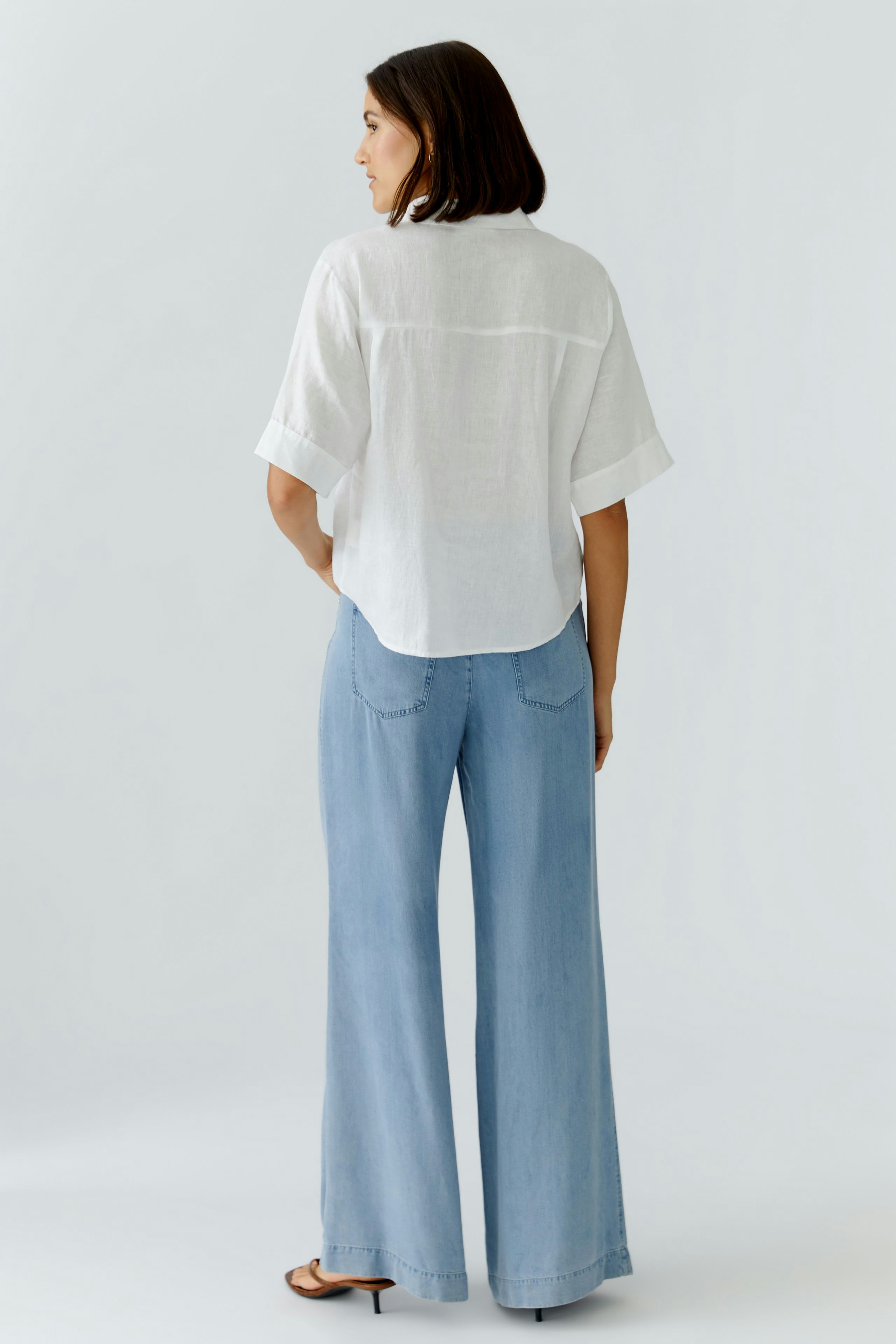 Casual women's blouse: A woman in a loose-fitting white blouse and wide-leg jeans, showcasing a relaxed style.