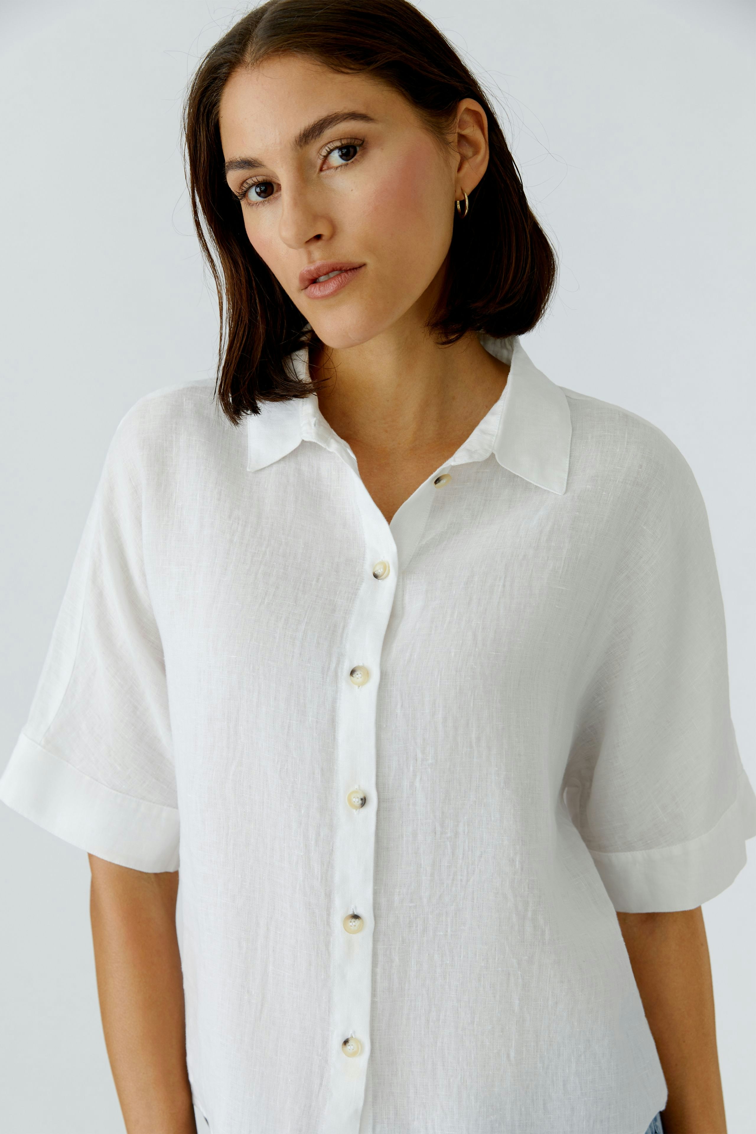 Casual women's blouse: A woman in a white button-up blouse with short sleeves, looking confidently.