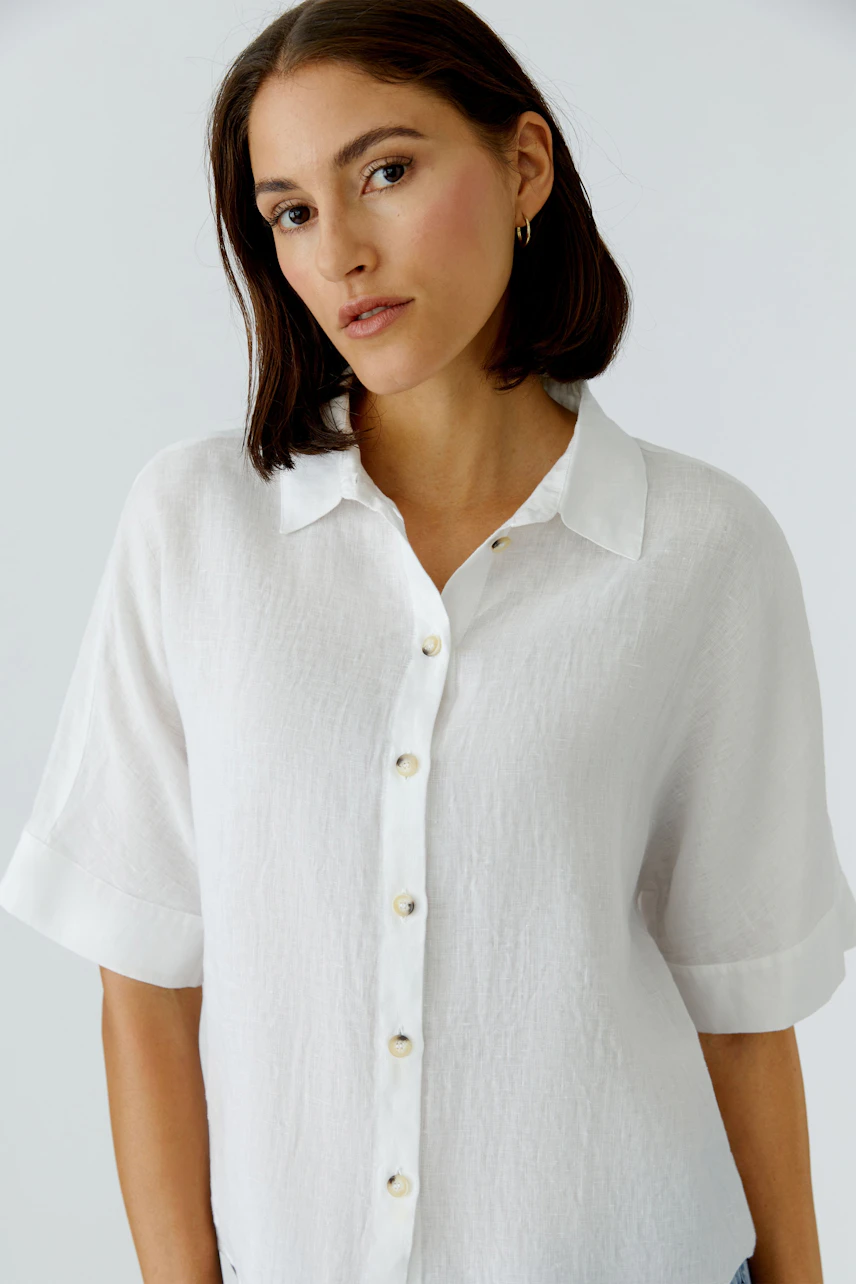 Casual women's blouse: A woman in a white button-up blouse with short sleeves, looking confidently.