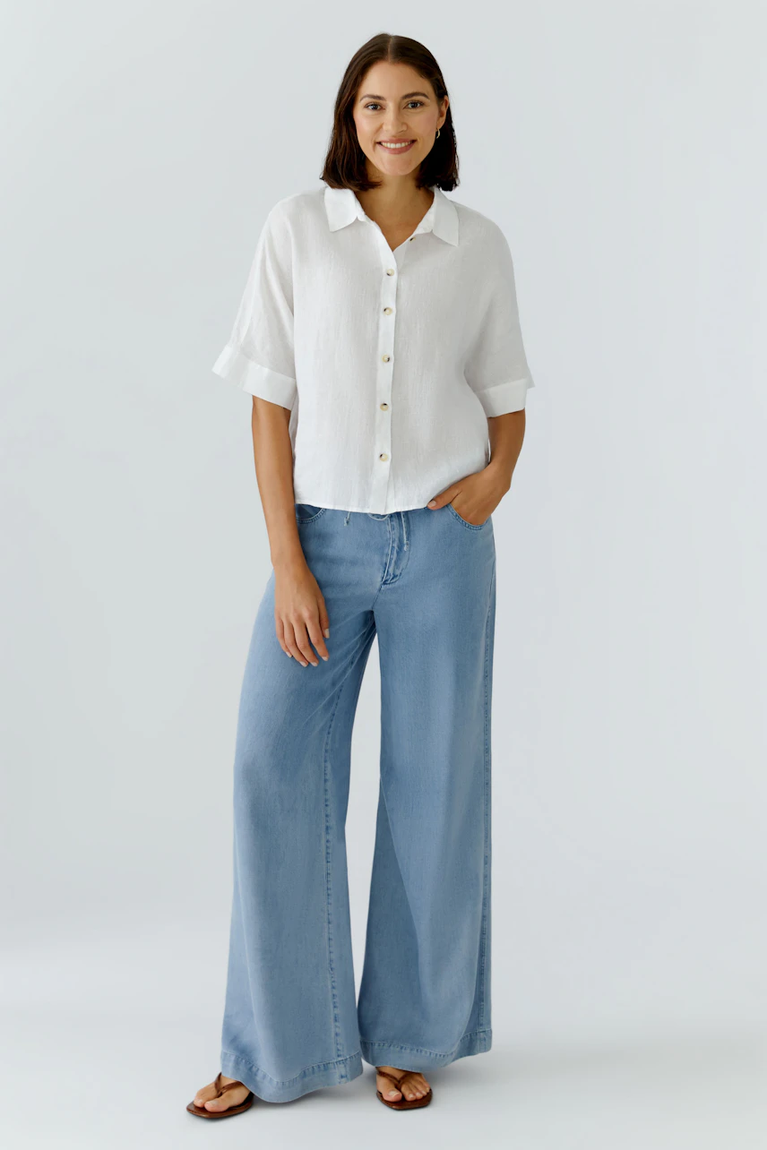 Casual women's blouse: A woman in a white button-up blouse and wide-leg jeans smiles confidently.