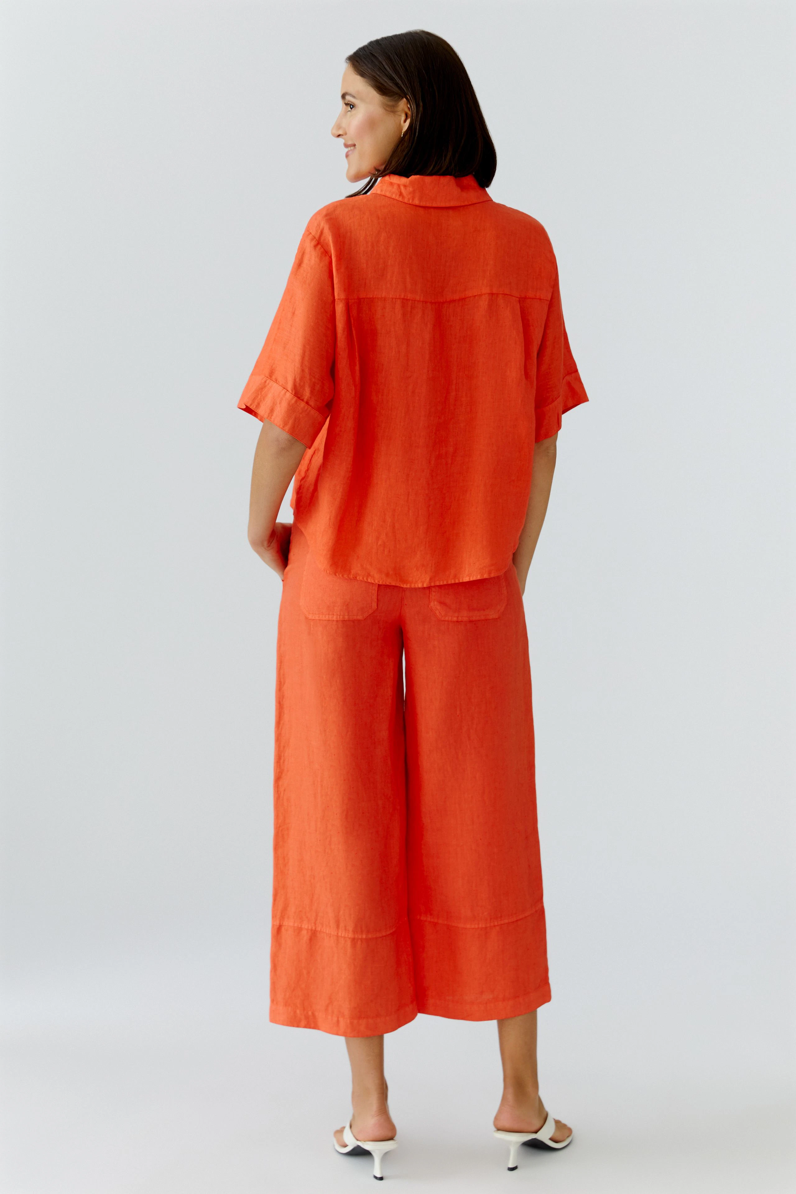 Lässige Damen-Bluse: Frau in orangefarbener Bluse mit lockerer Passform und kurzen Ärmeln von hinten.